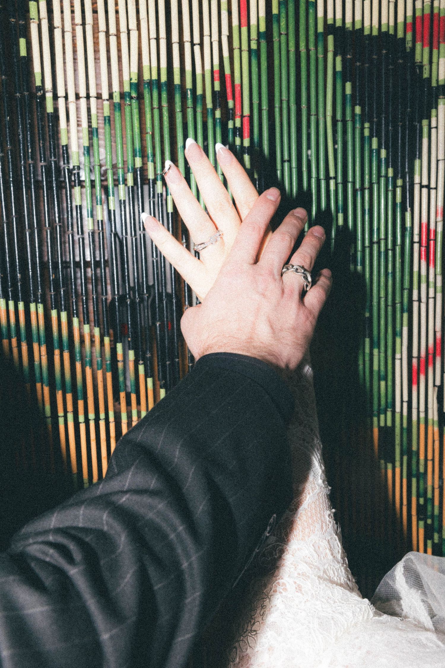 Hand with silver rings pressed against a colorful bamboo beaded curtain backdrop.