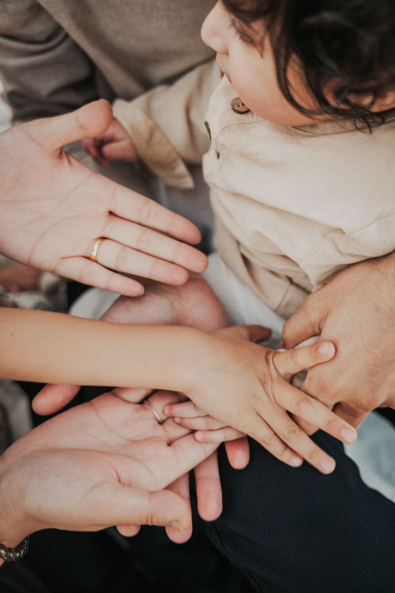 Close-up of family hands stacked together showing wedding ring and baby hands.