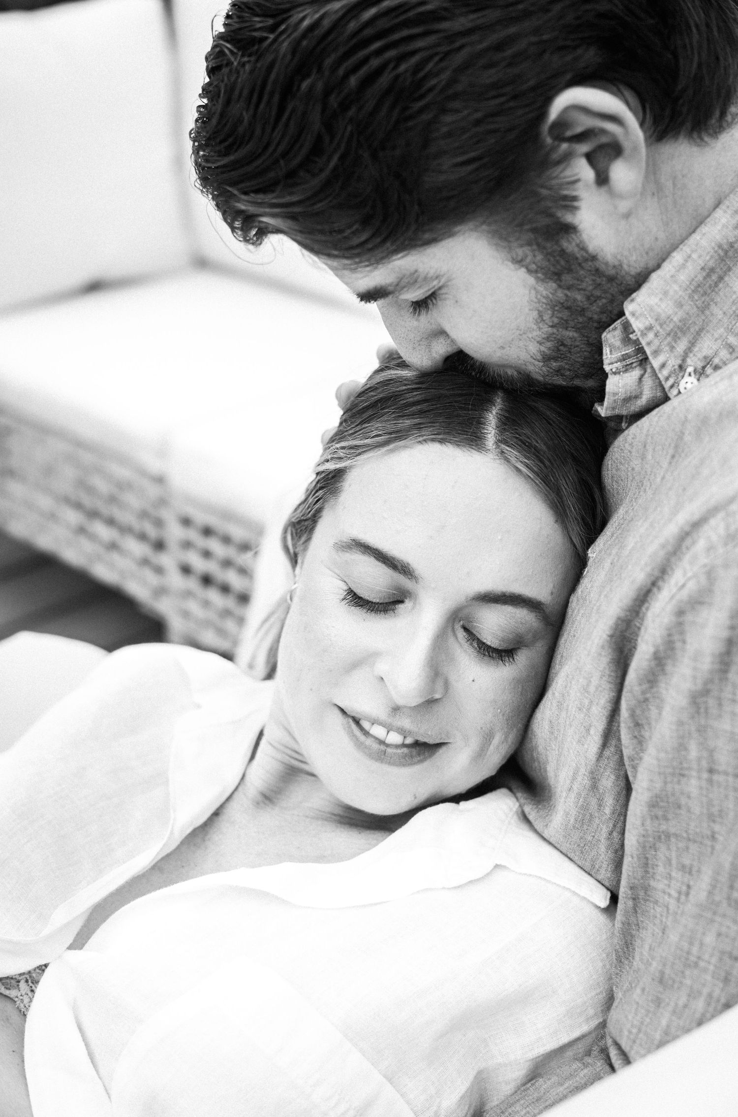 Black and white photo of a couple embracing tenderly, woman resting her head on man's chest with eyes closed.