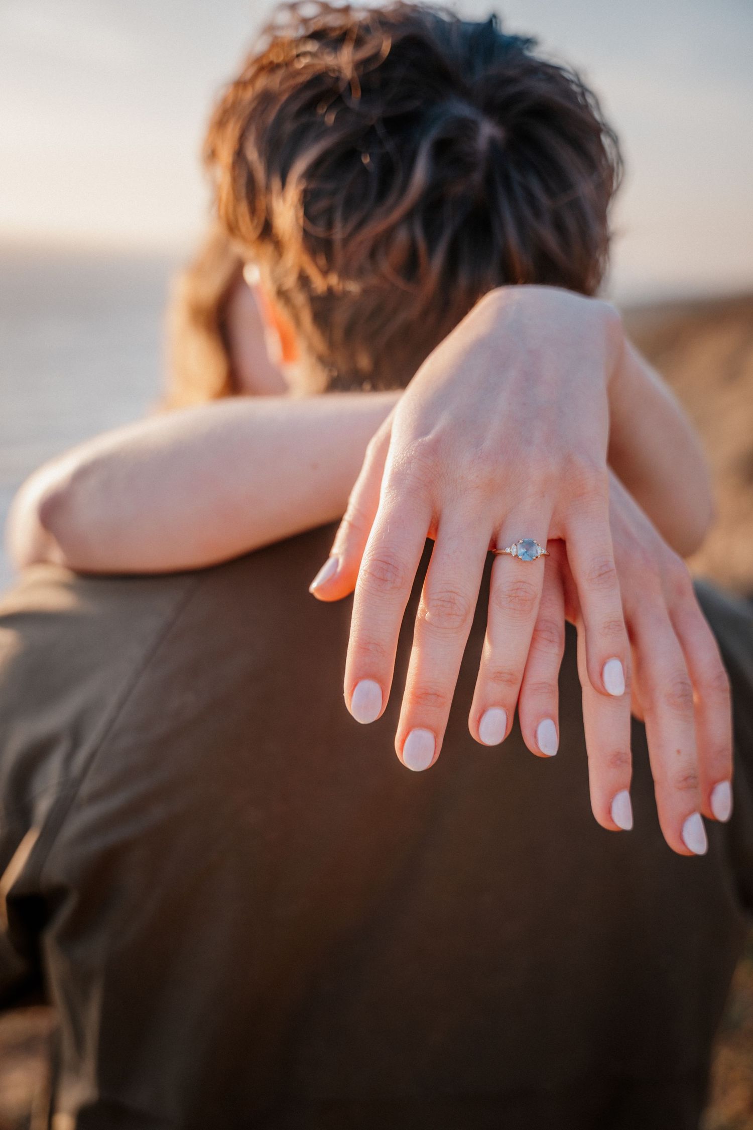 Close-up of a woman showing off her diamond engagement ring while embracing her partner.