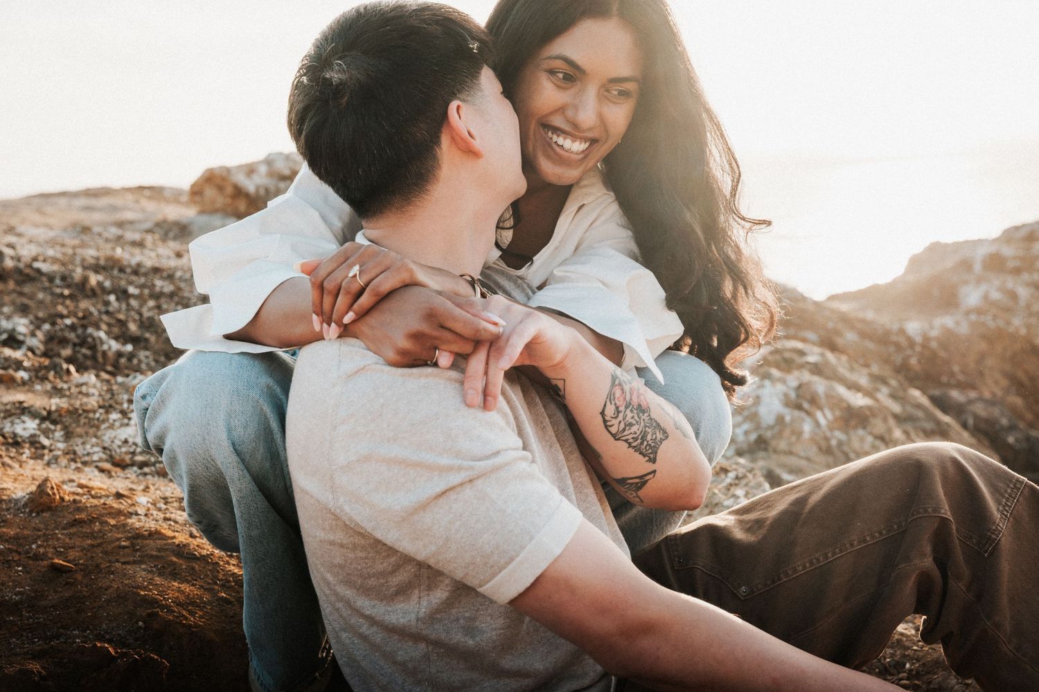 A couple shares a romantic moment outdoors, with the woman smiling as she embraces a man against a rocky backdrop.
