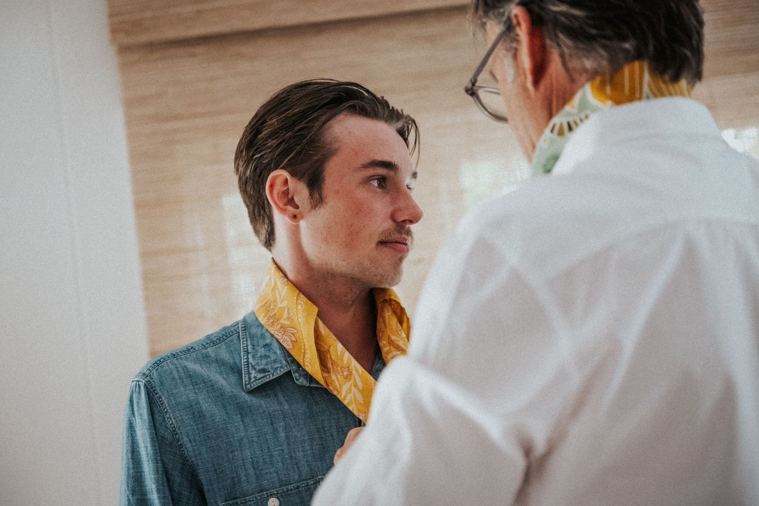 Two men in stylish attire having a conversation, one wearing a denim jacket with yellow collar detail.