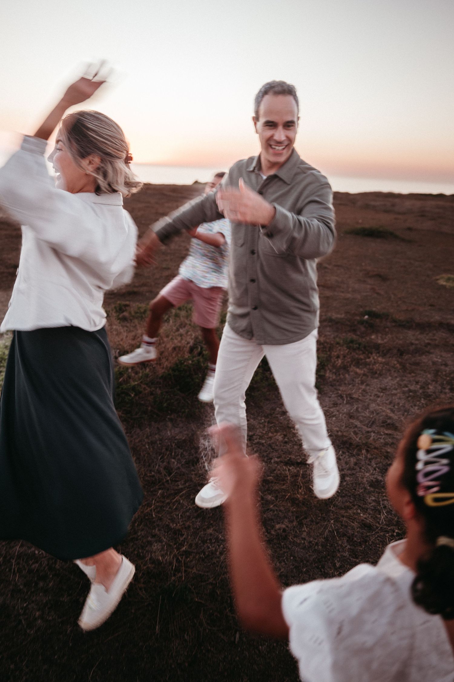 A joyful family dances together on an open field during a vibrant sunset.