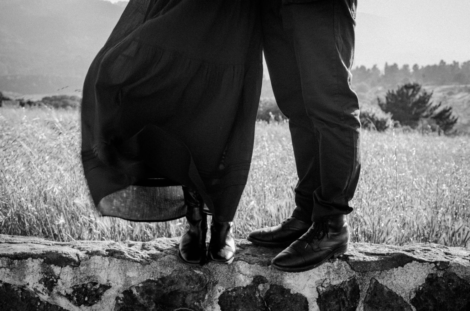 Black and white photo of a couple standing on rocks in a field, wearing formal attire.Photography by The Y.K. Studio.