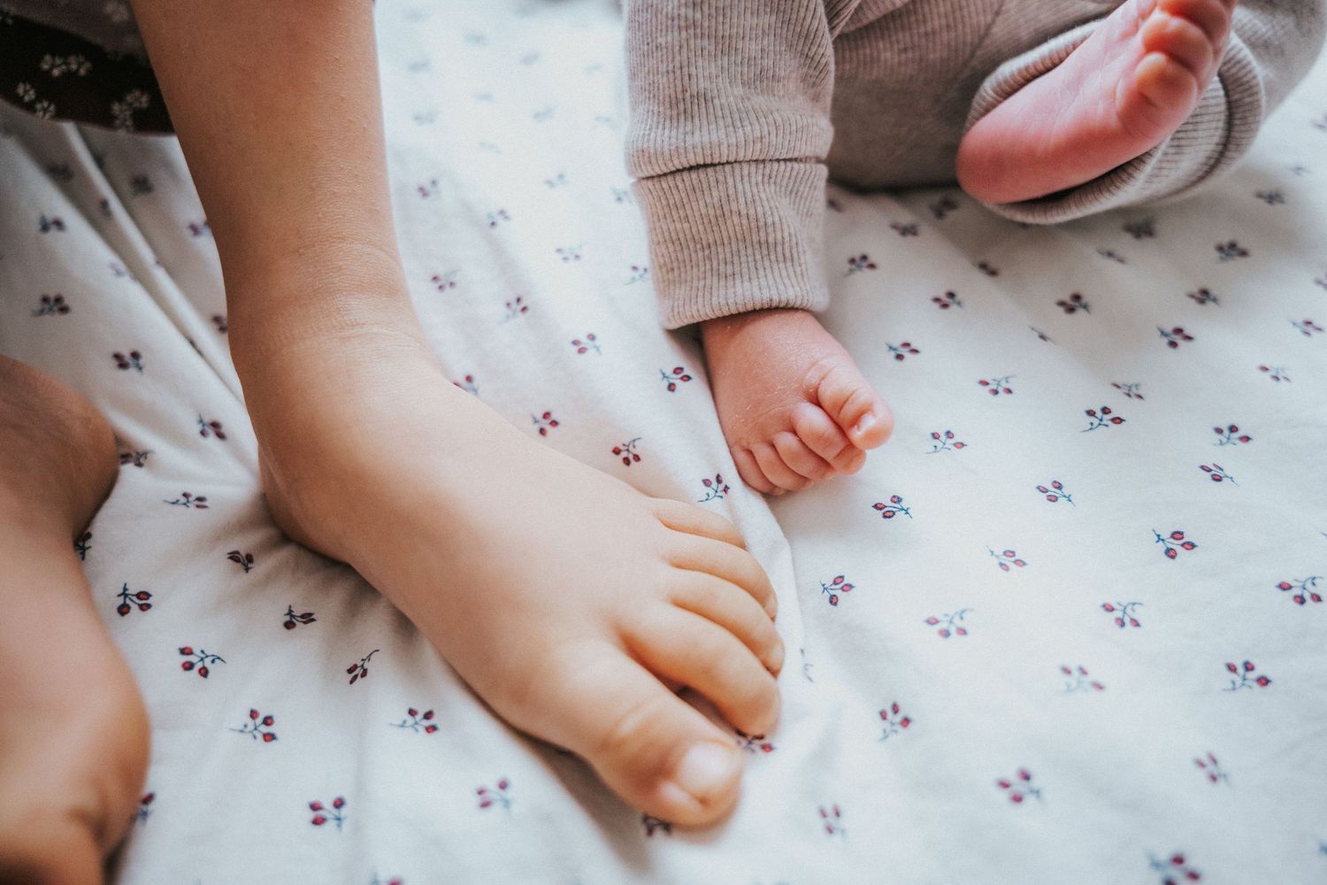 Close-up of a toddler and newborn baby feet resting on a white floral patterned blanket.