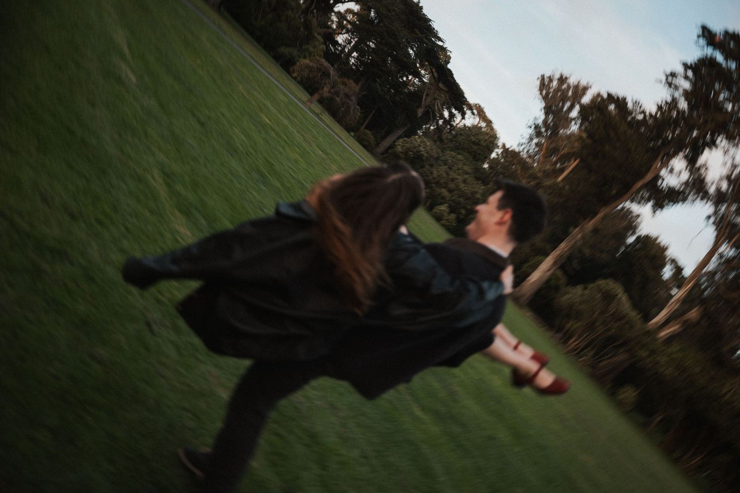 Couple dancing and spinning together on a lush green lawn with trees in the background.Photography by The Y.K. Studio.