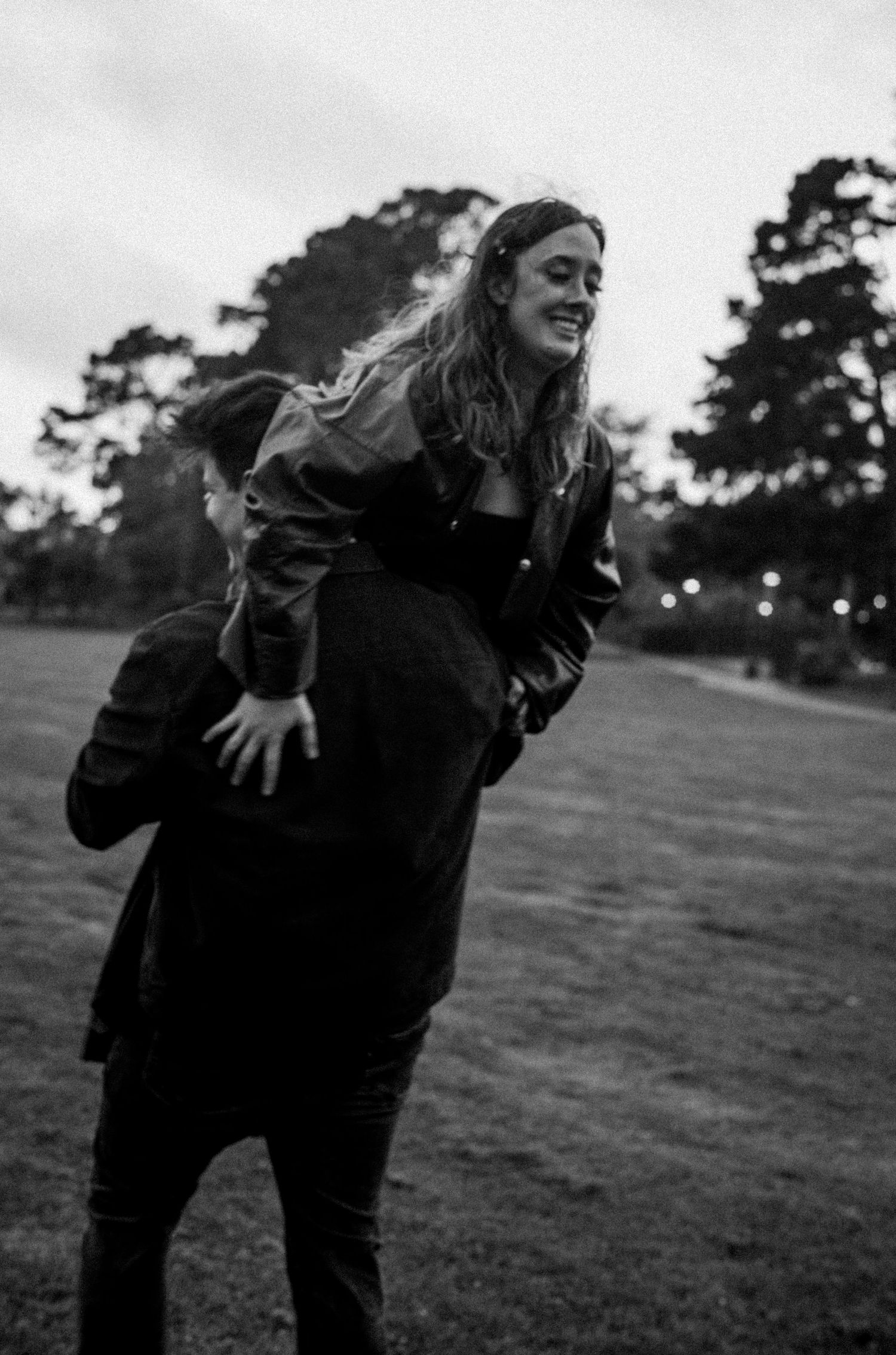 Joyful woman laughing while being carried piggyback in a black and white outdoor park photo.