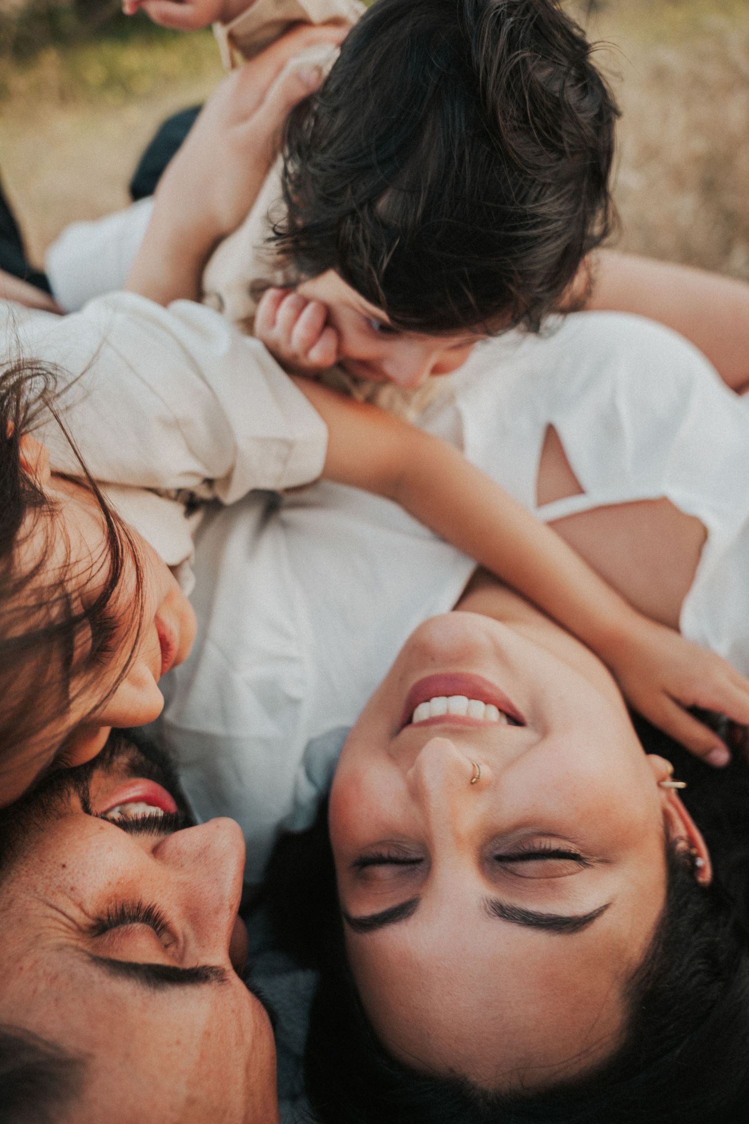 Three women laughing and lying on the ground together, enjoying a joyful candid moment outdoors.