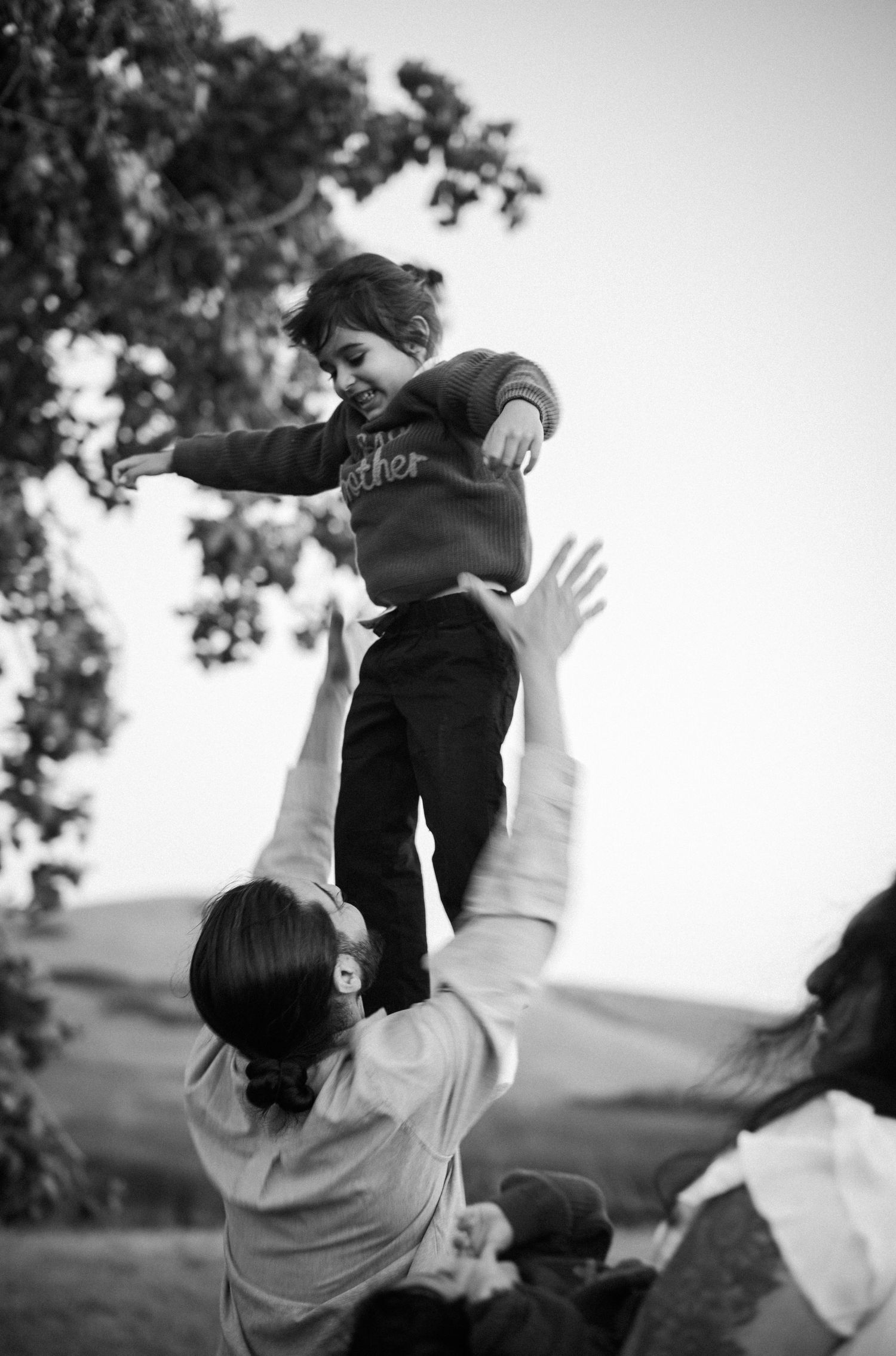Black and white photo of parent joyfully tossing laughing child into the air outdoors.