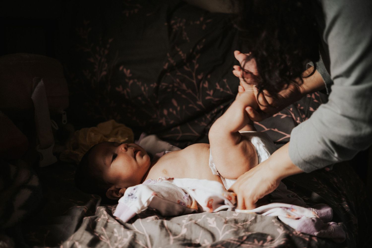 A newborn baby lying on a blanket while a caregiver gently holds its tiny feet in a dimly lit room.