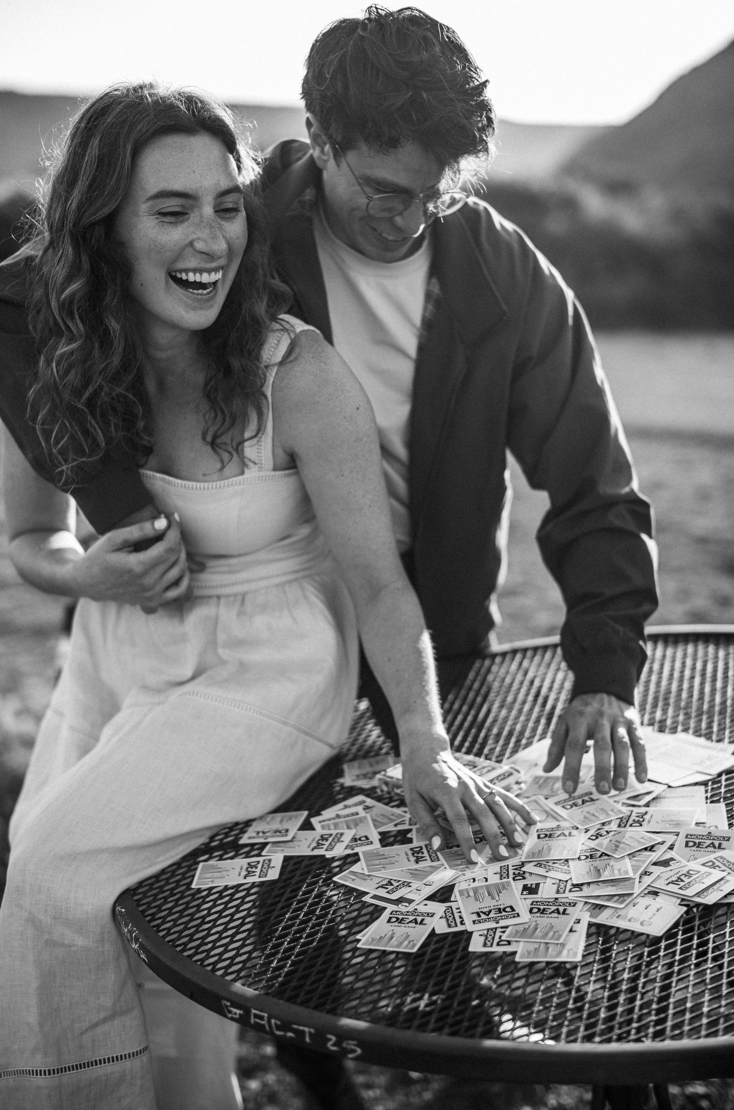 Black and white photo of a laughing couple looking at lottery tickets spread on an outdoor metal table.