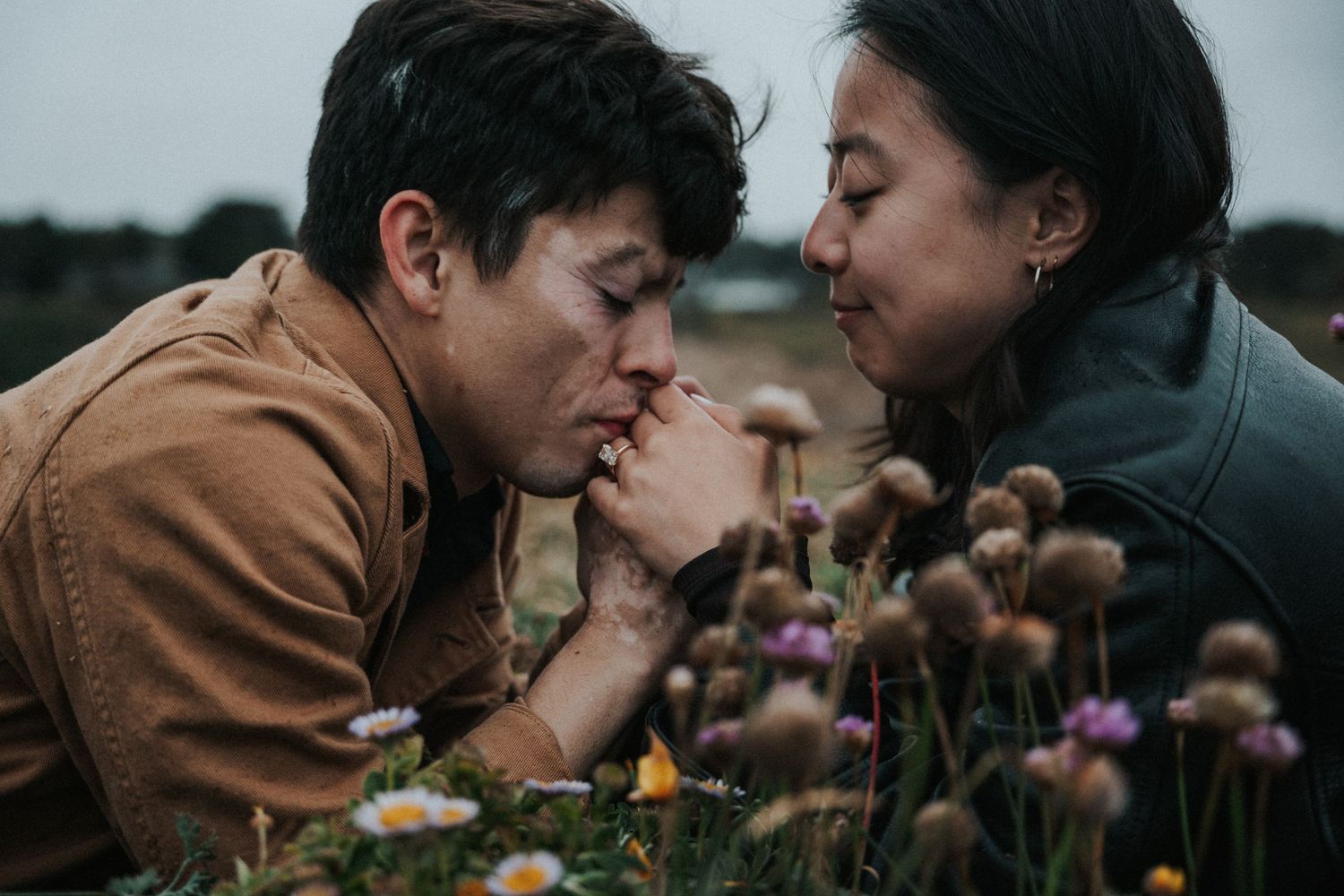 Couple lying in a flower field, man gently kissing woman's hand among wildflowers.
