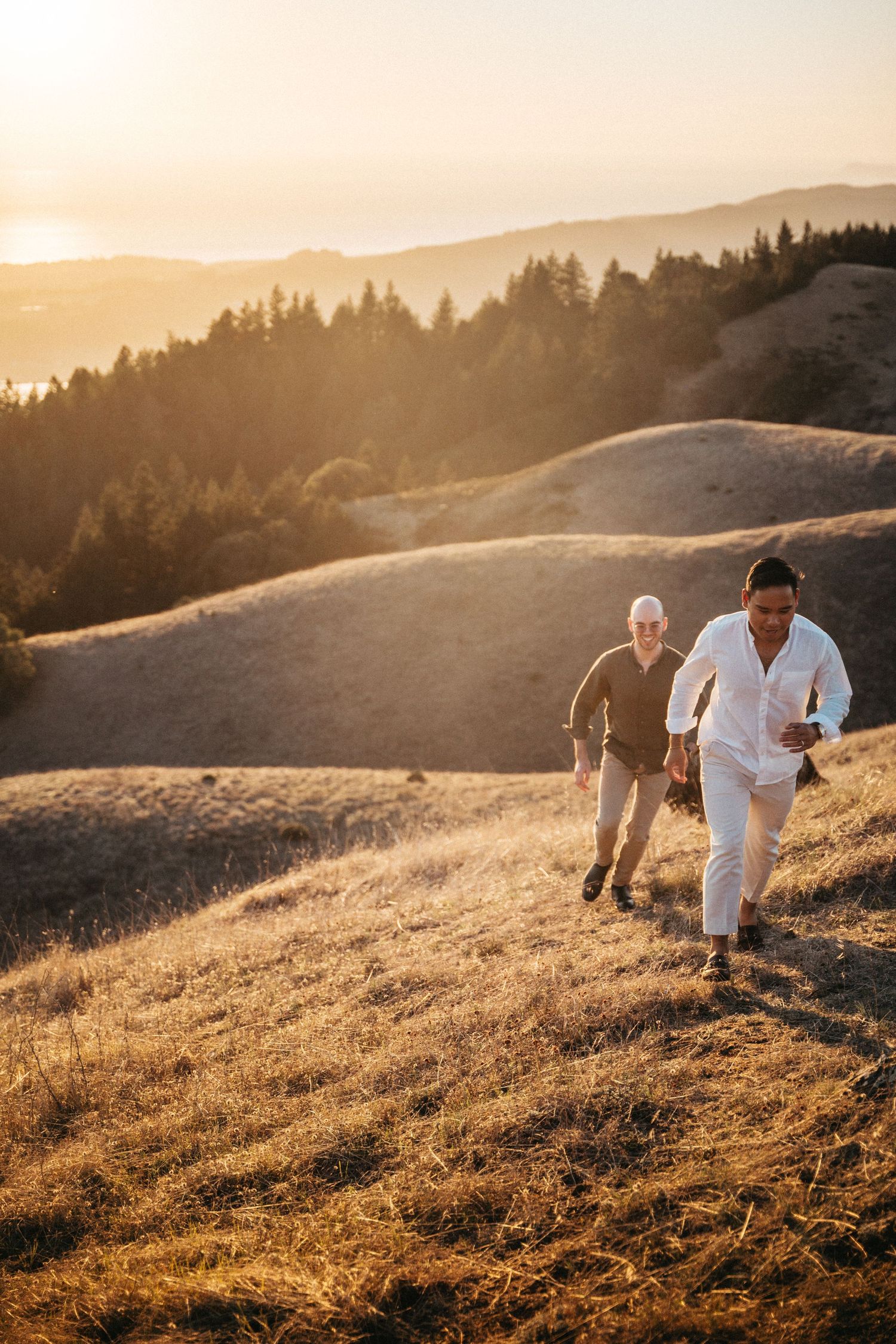 Two men hiking up golden hills at sunset with mountain views.