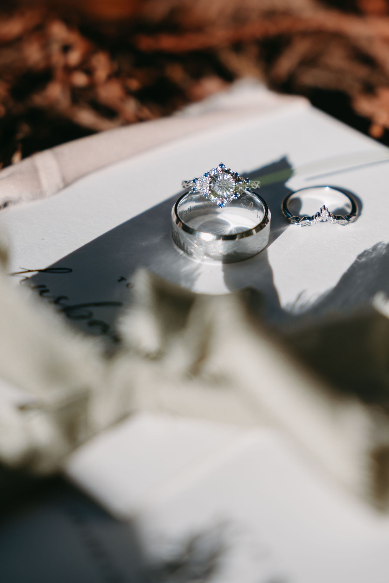 Three silver wedding rings with diamonds displayed on white paper, with soft natural light and bokeh background.