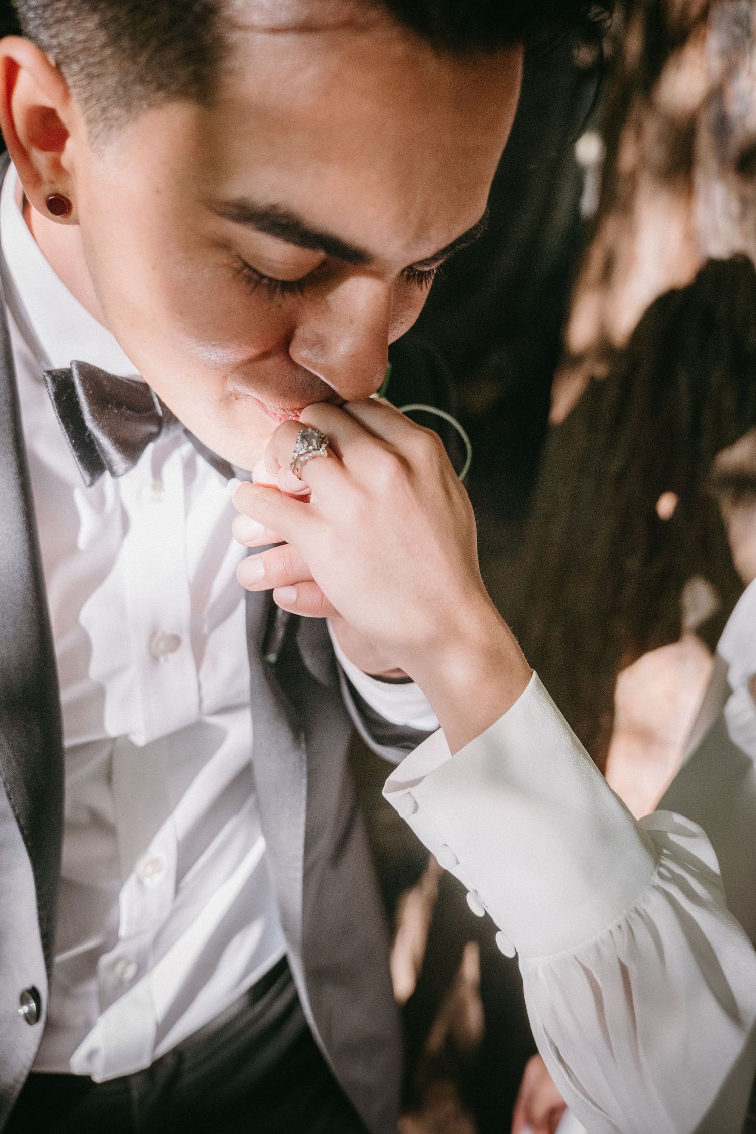 Groom in gray suit kissing bride's hand adorned with elegant ring at wedding ceremony.
