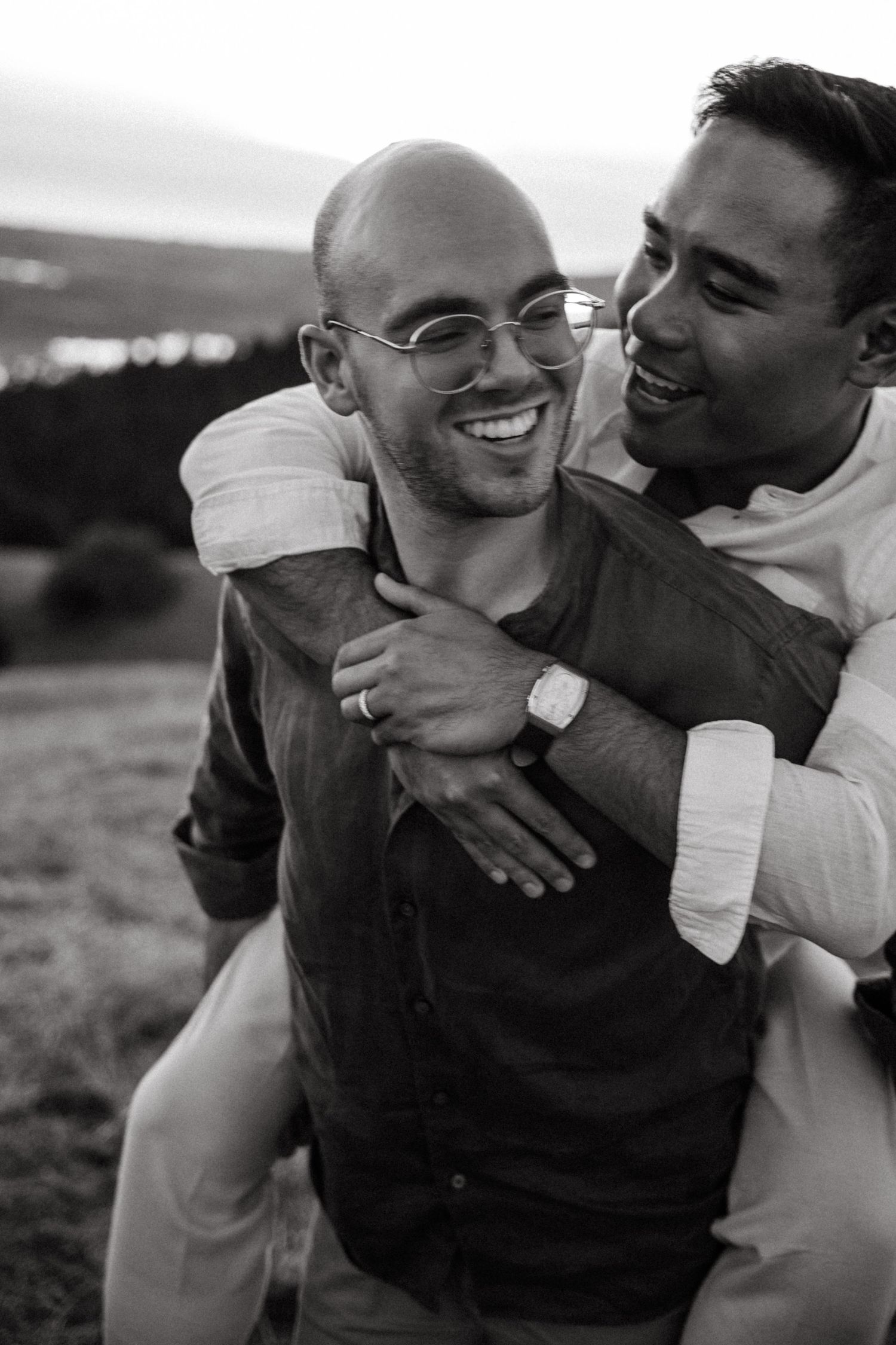 Two smiling men sharing a joyful piggyback moment in a black and white outdoor couples portrait.