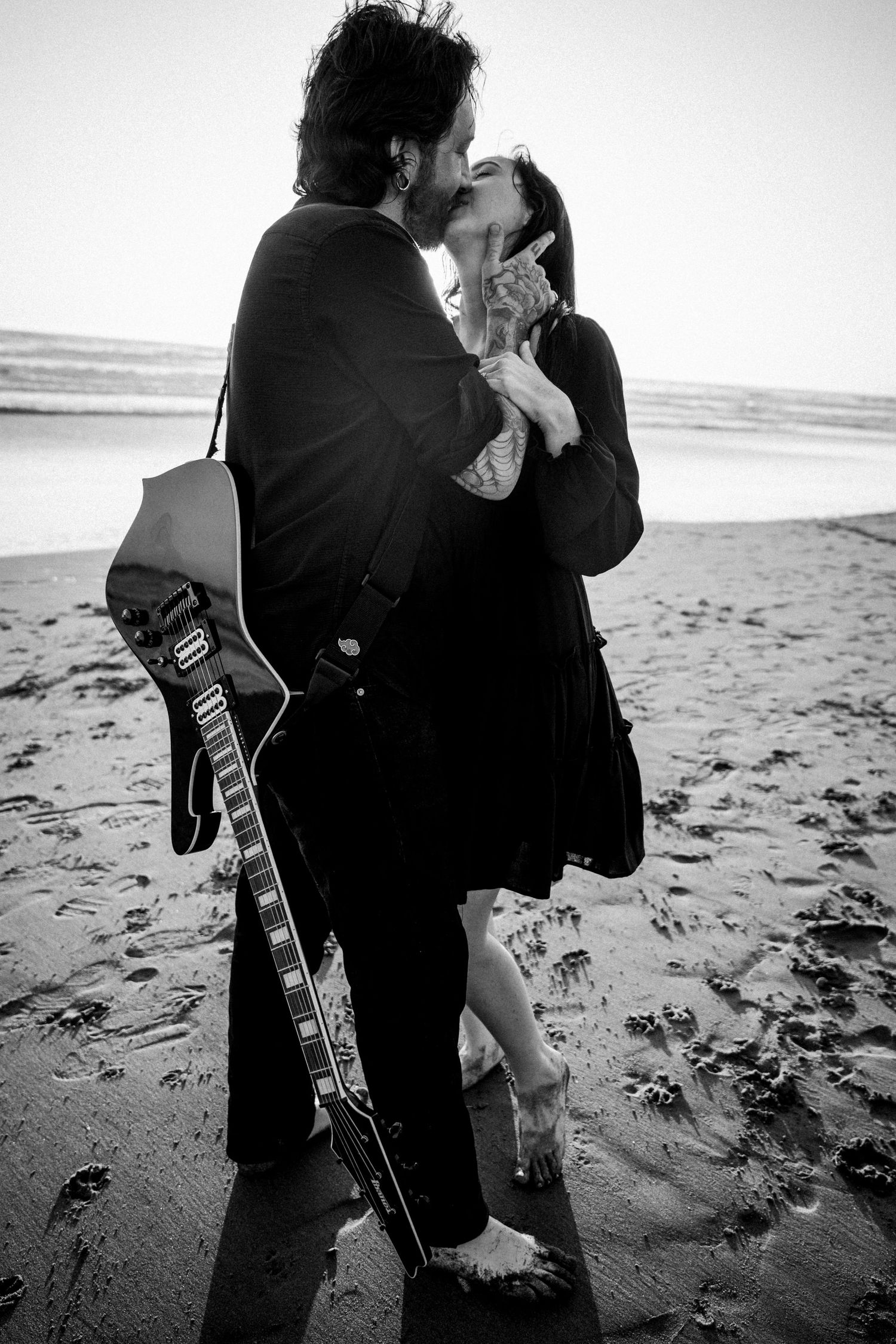 Couple kissing on beach with man holding electric guitar in black and white.