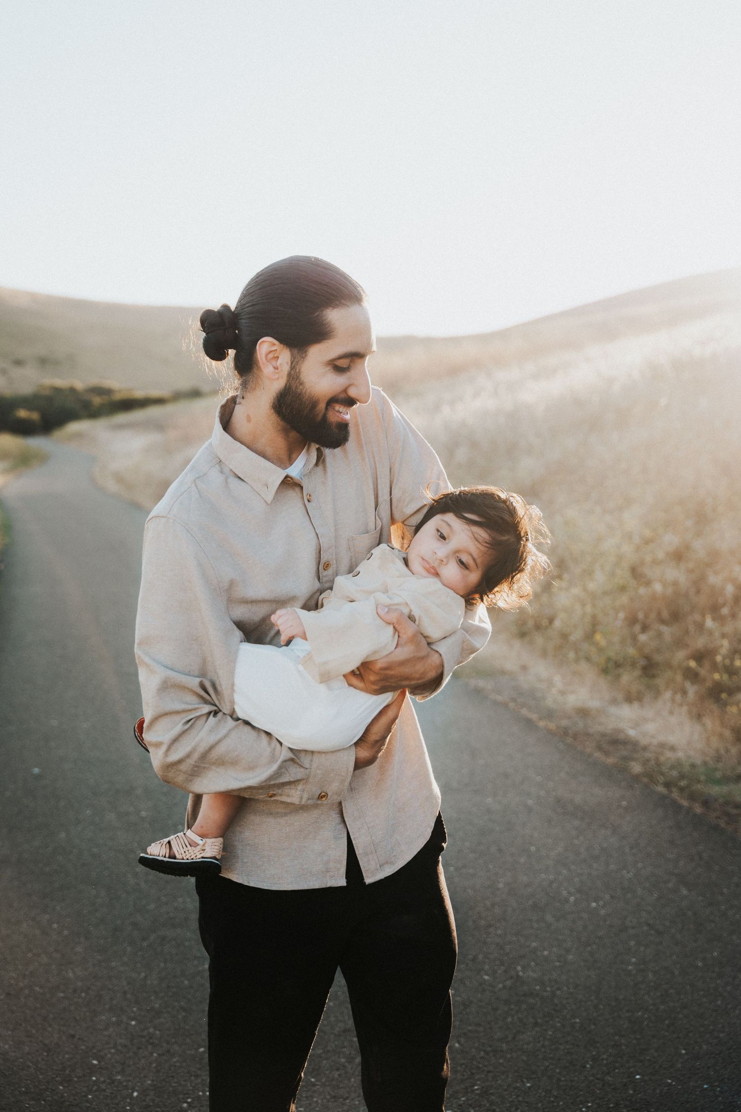Bearded father with man bun lovingly holds his baby on a scenic outdoor path.