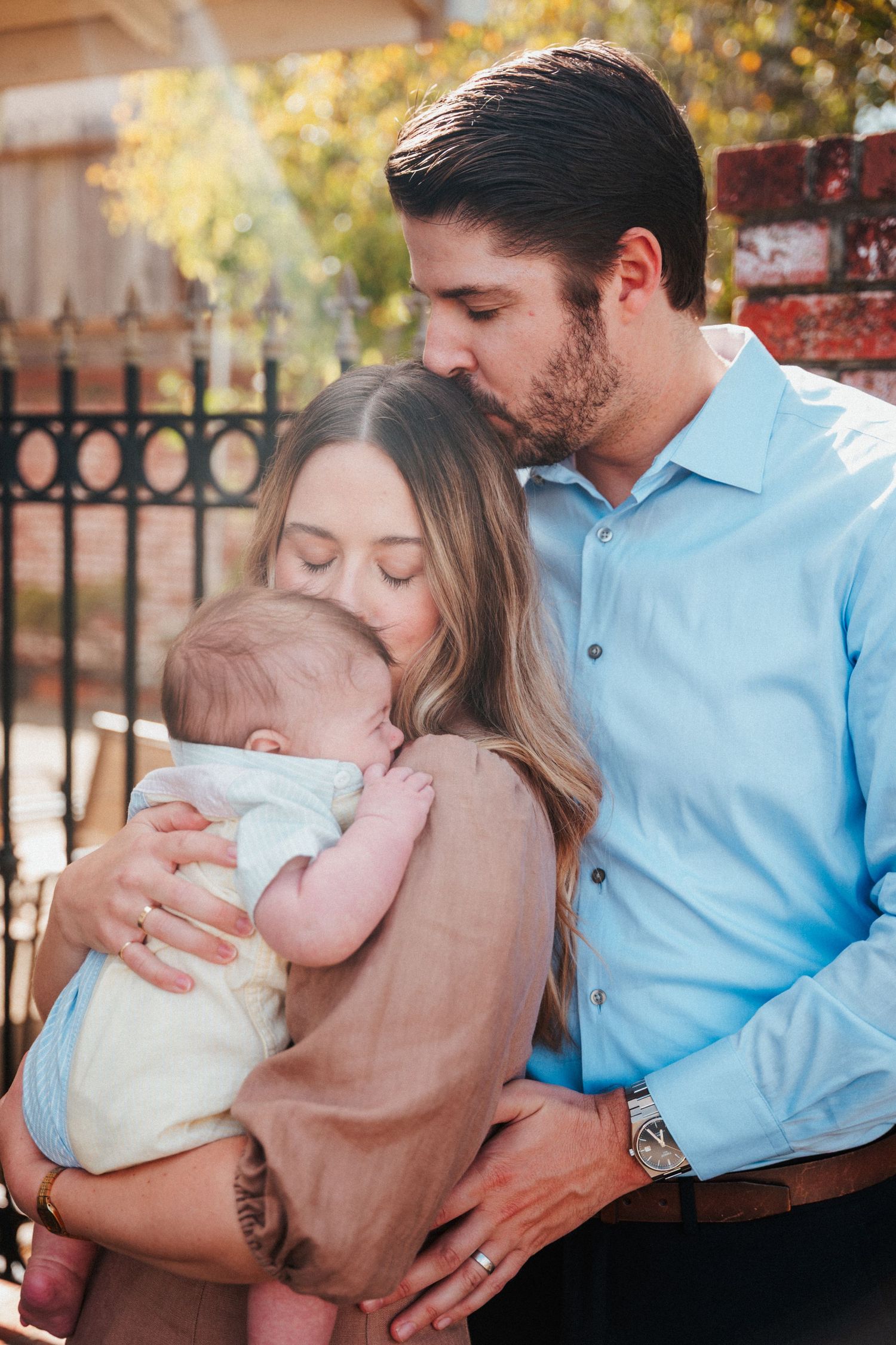 A couple shares a tender moment, the man kissing the woman's head as she holds their newborn.