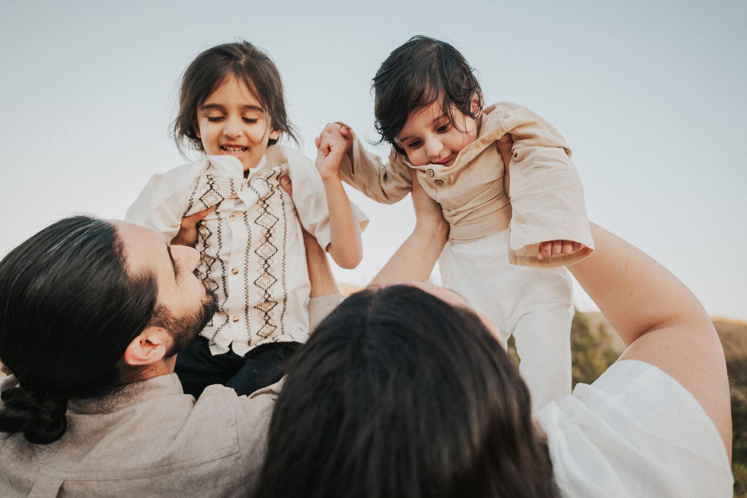Parents joyfully lifting two young children outdoors against a clear sky in a heartwarming family moment.