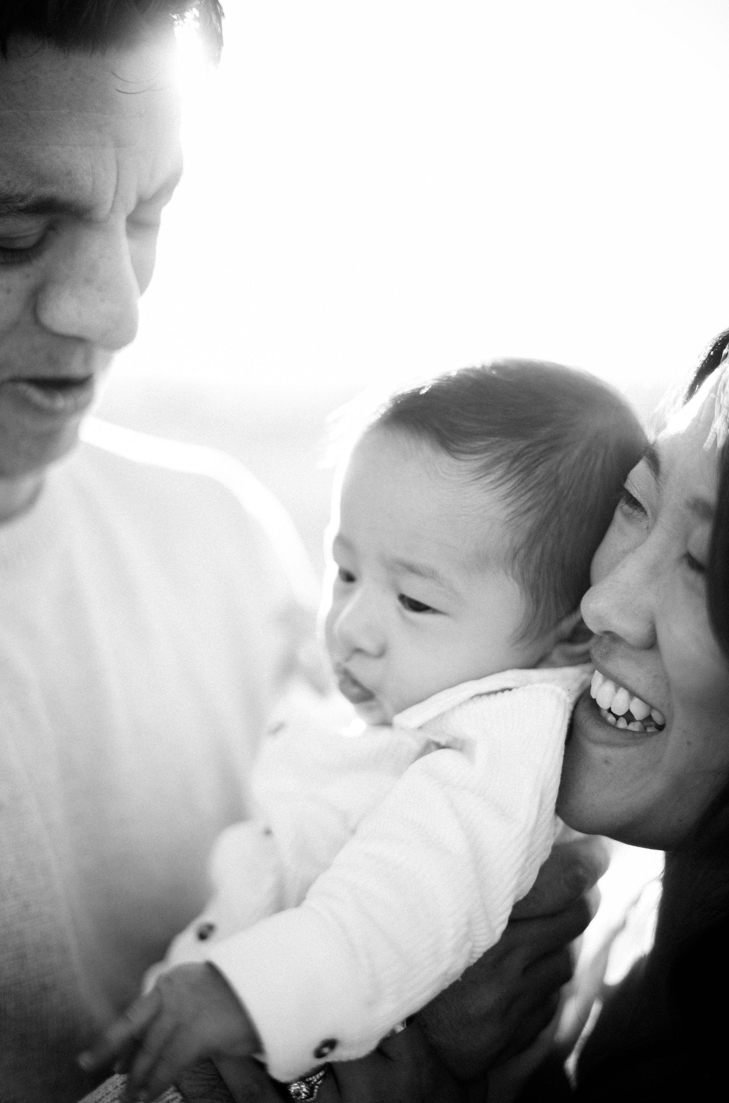 Black and white photo of smiling parents lovingly holding their newborn baby together.