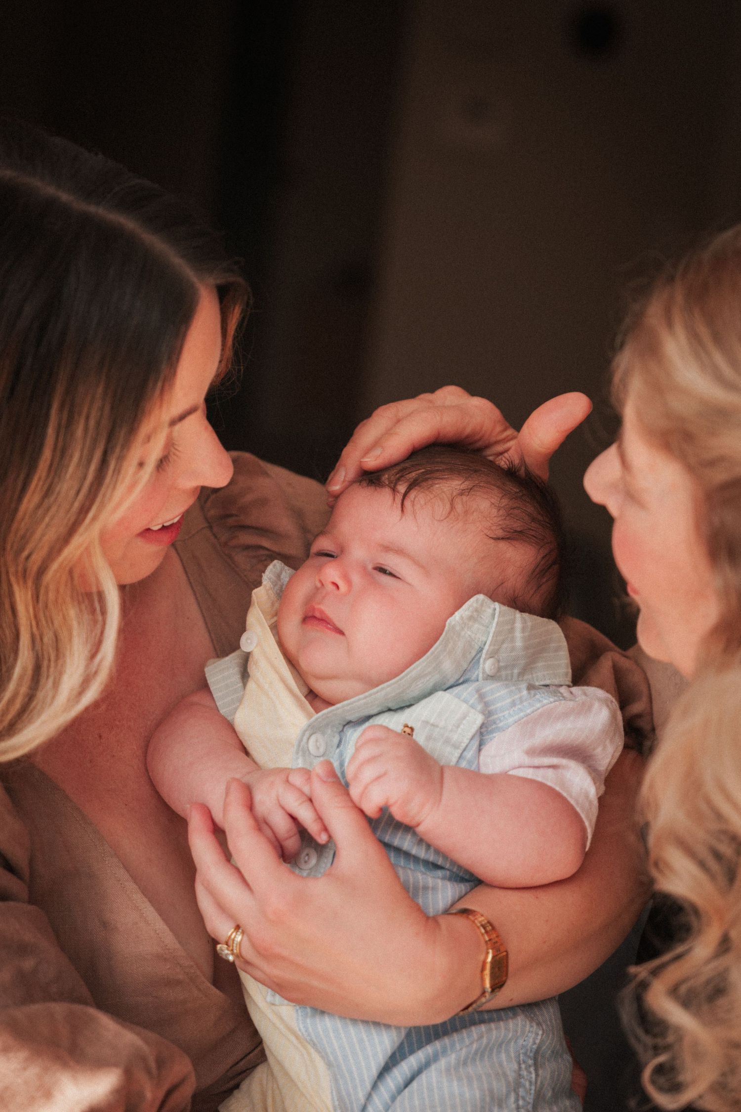 Two women lovingly cradle a newborn baby, gently touching his head indoors.