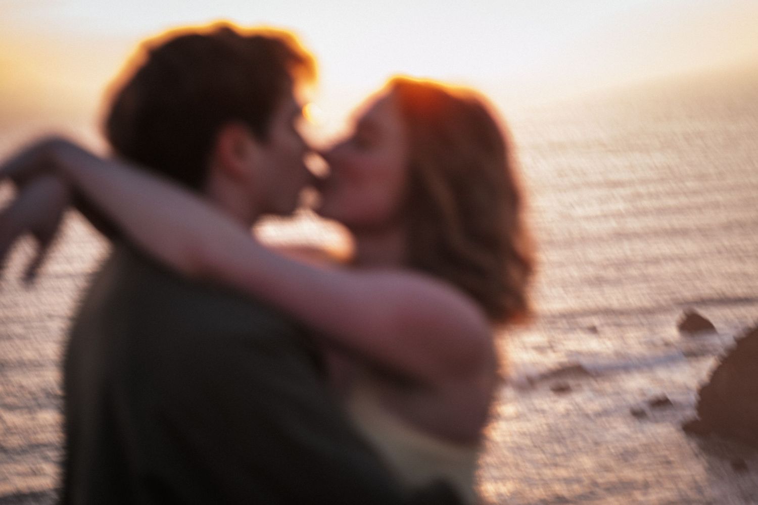 Romantic couple kissing at sunset on a beach, warm golden light glowing behind them.