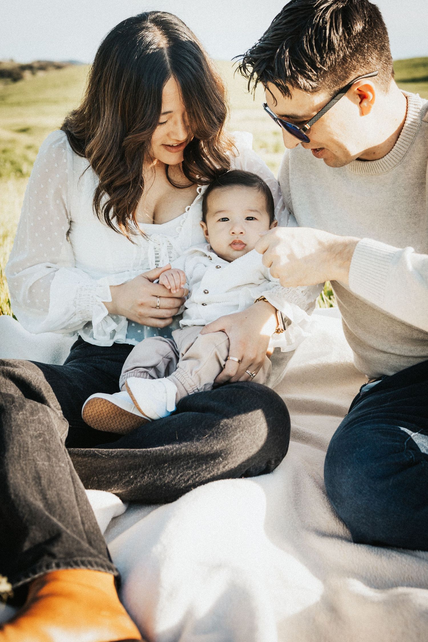 Young family sitting on blanket outdoors in golden sunlight with baby in mothers lap.