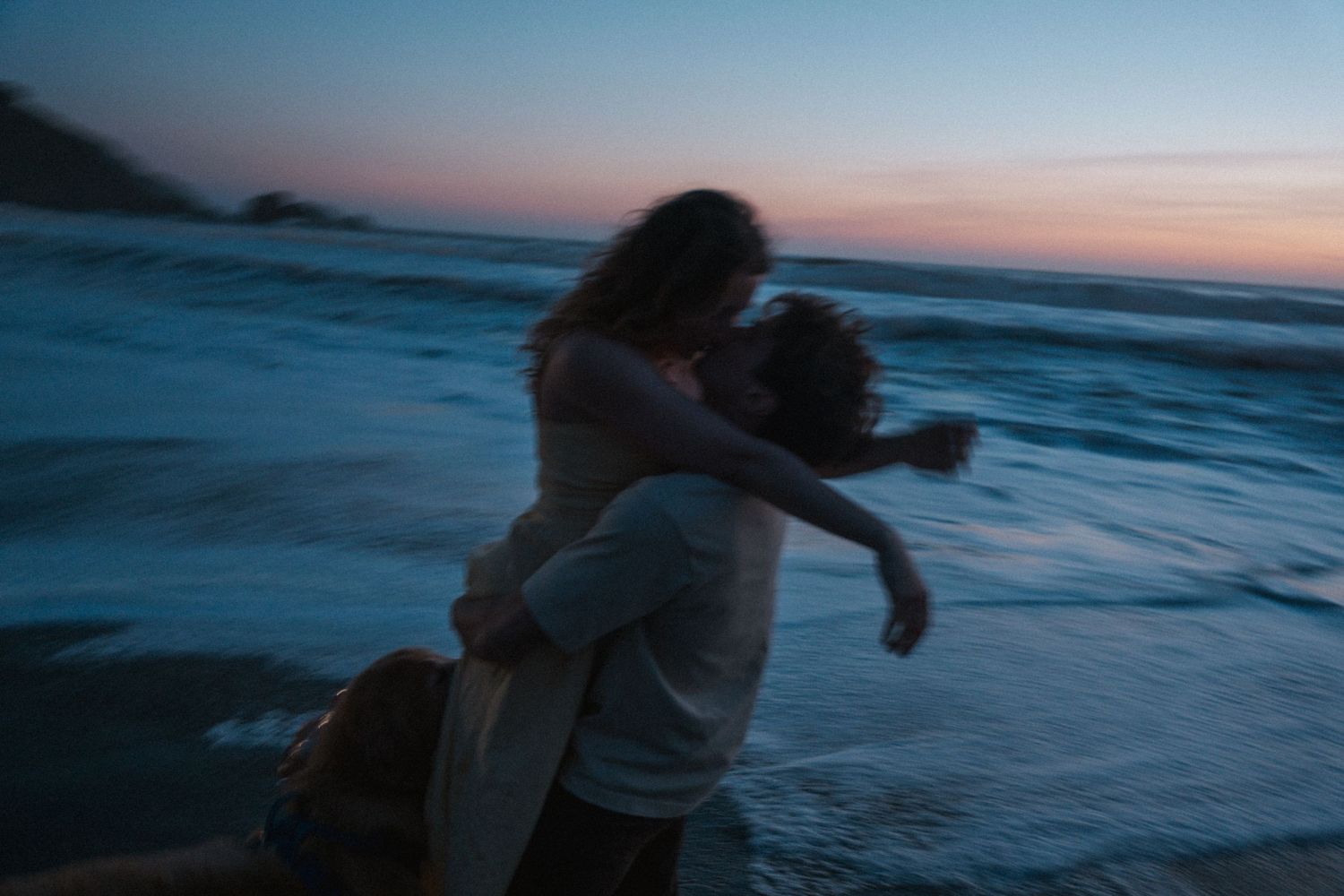 Romantic couple embracing and spinning on a beach at sunset with ocean waves in the background. Photography by The Y.K. Studio.