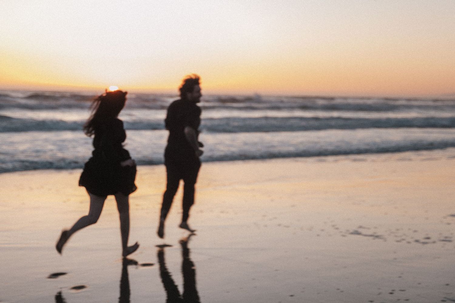Two people running along a beach at sunset, silhouetted against golden ocean waves.