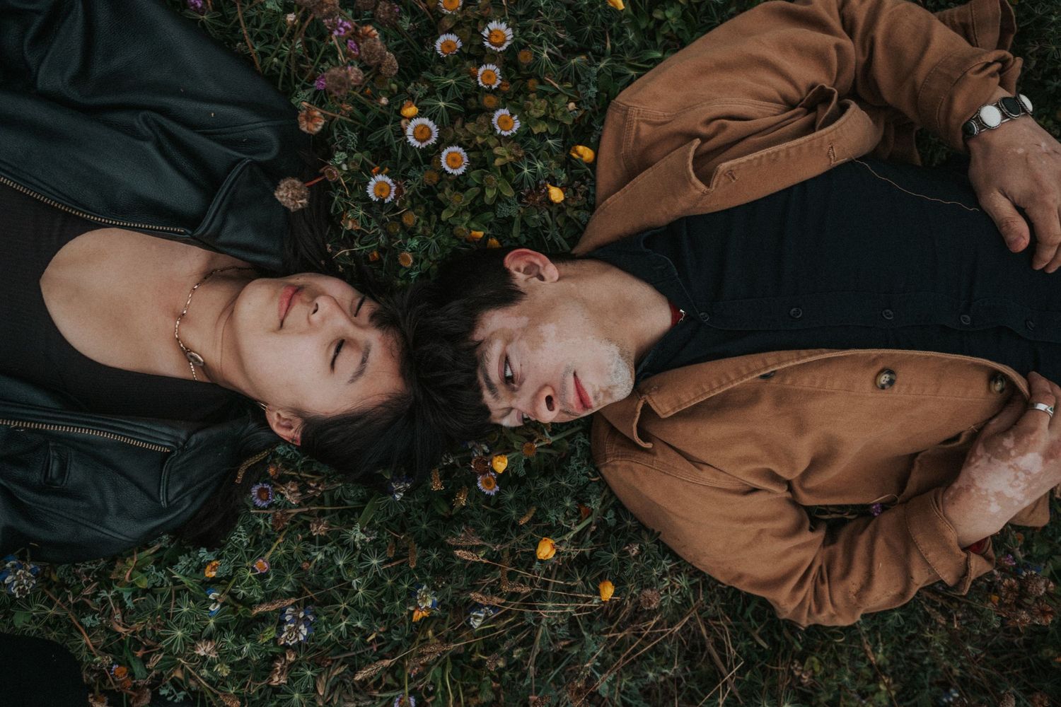 Romantic couple lying together on a flower meadow, faces close, surrounded by colorful wildflowers.