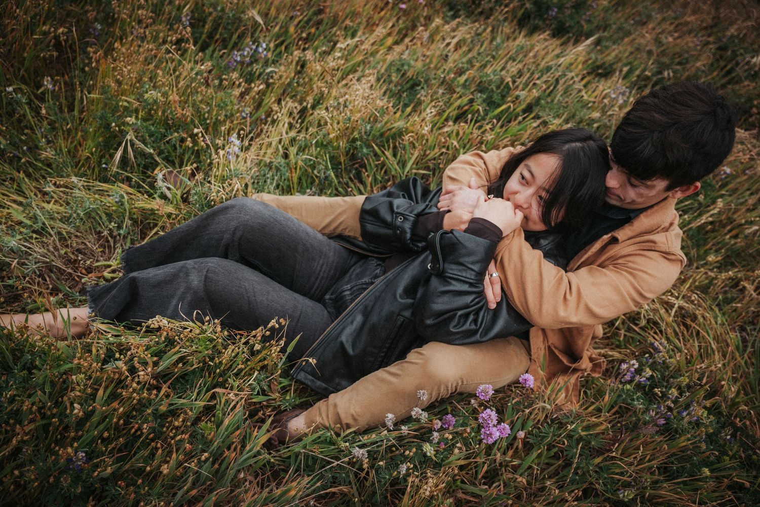 Romantic couple lying together in a grassy meadow surrounded by wildflowers.