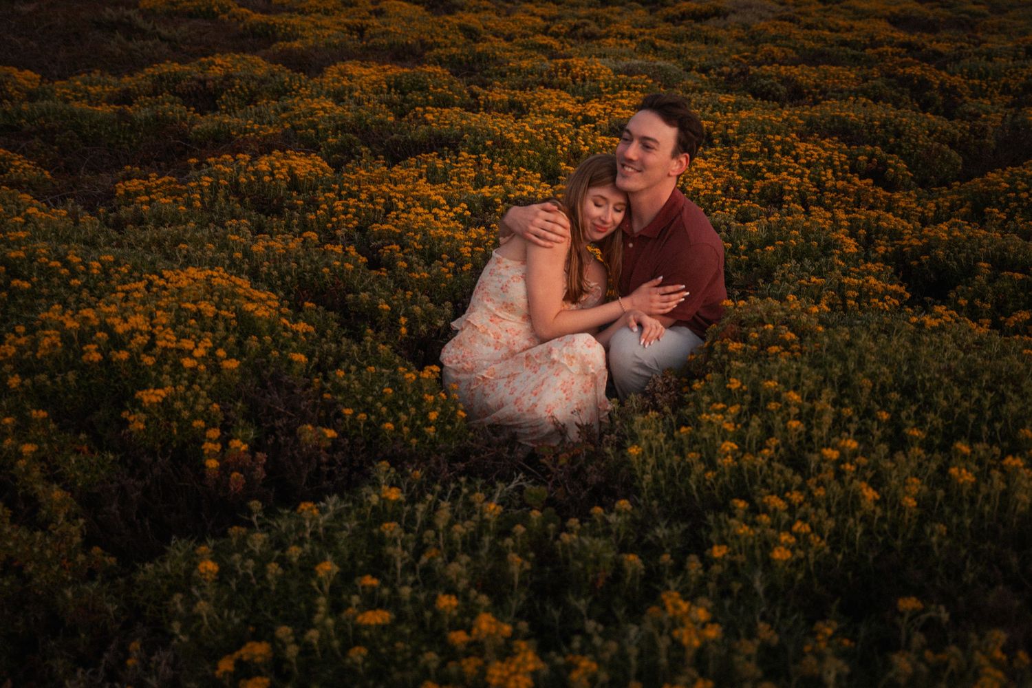 Couple embracing in a golden field of yellow wildflowers during sunset, sharing a romantic outdoor moment.