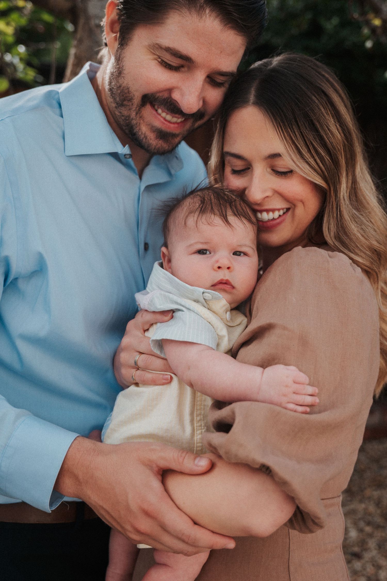Smiling couple holding their newborn baby outdoors, sharing a joyful family moment together.