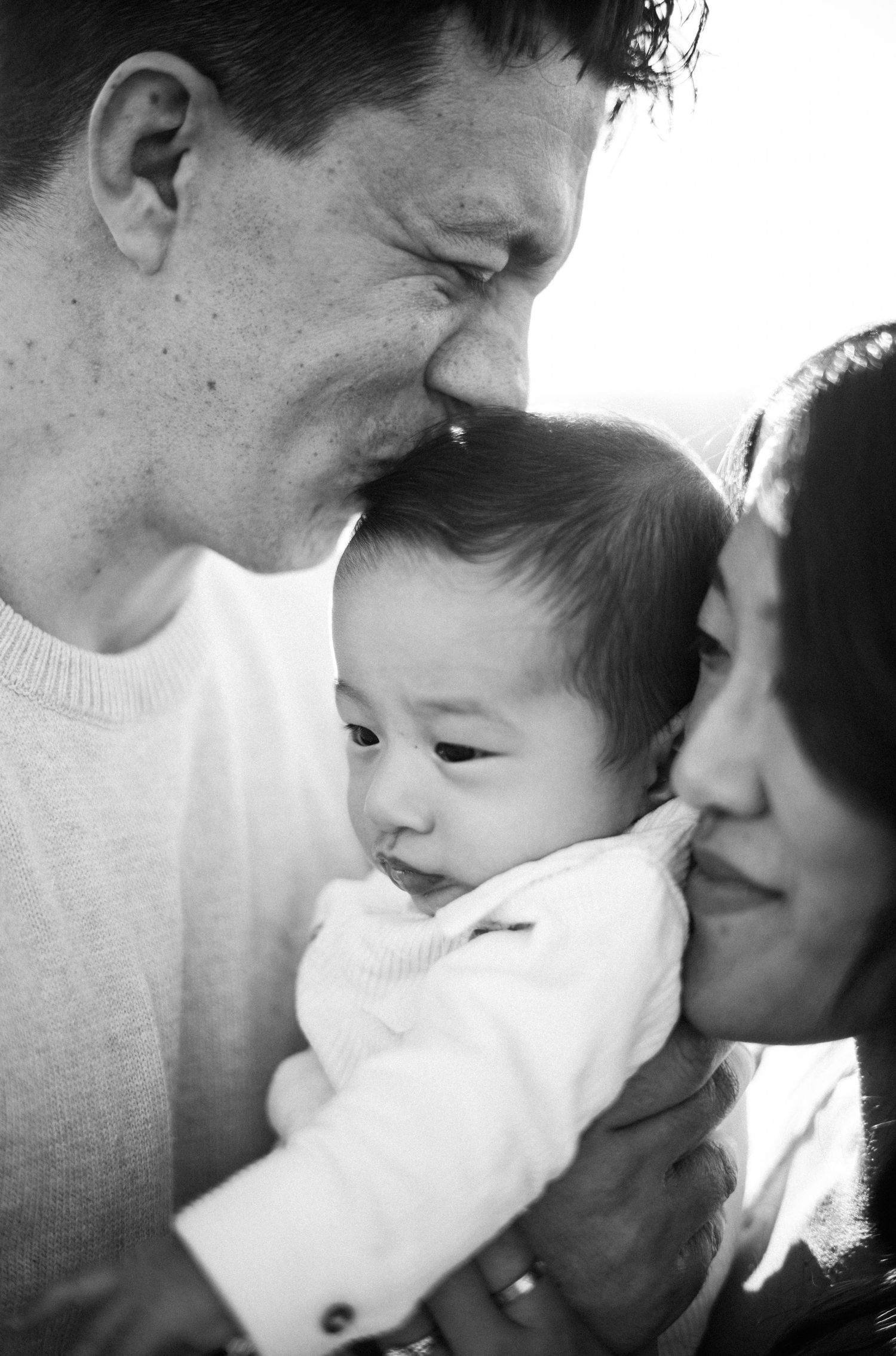 Black and white photo of loving parents kissing their newborn baby on both cheeks simultaneously.