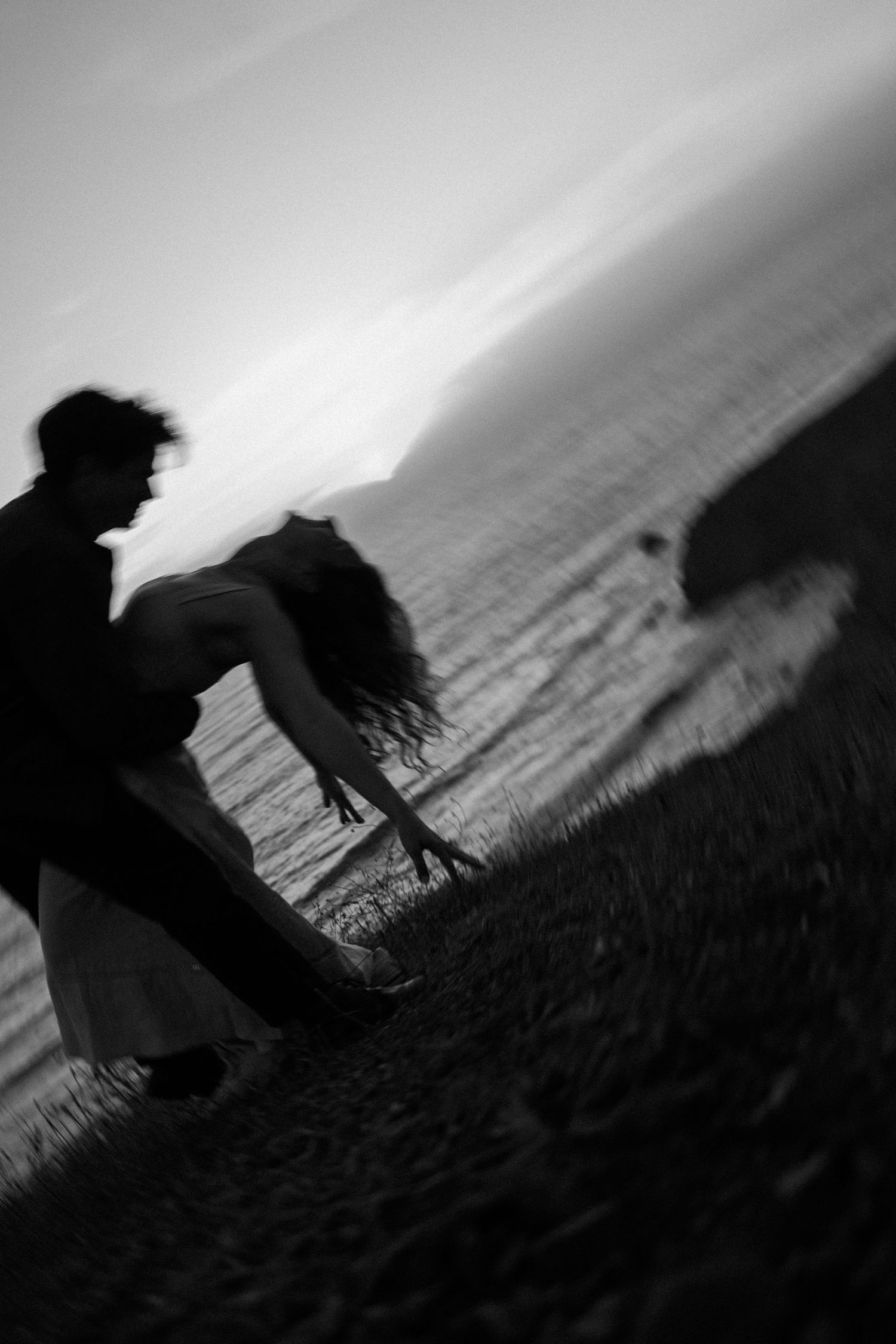 Blurred black and white photo of a couple dancing on a coastal hillside at dusk. Photography by The Y.K. Studio.