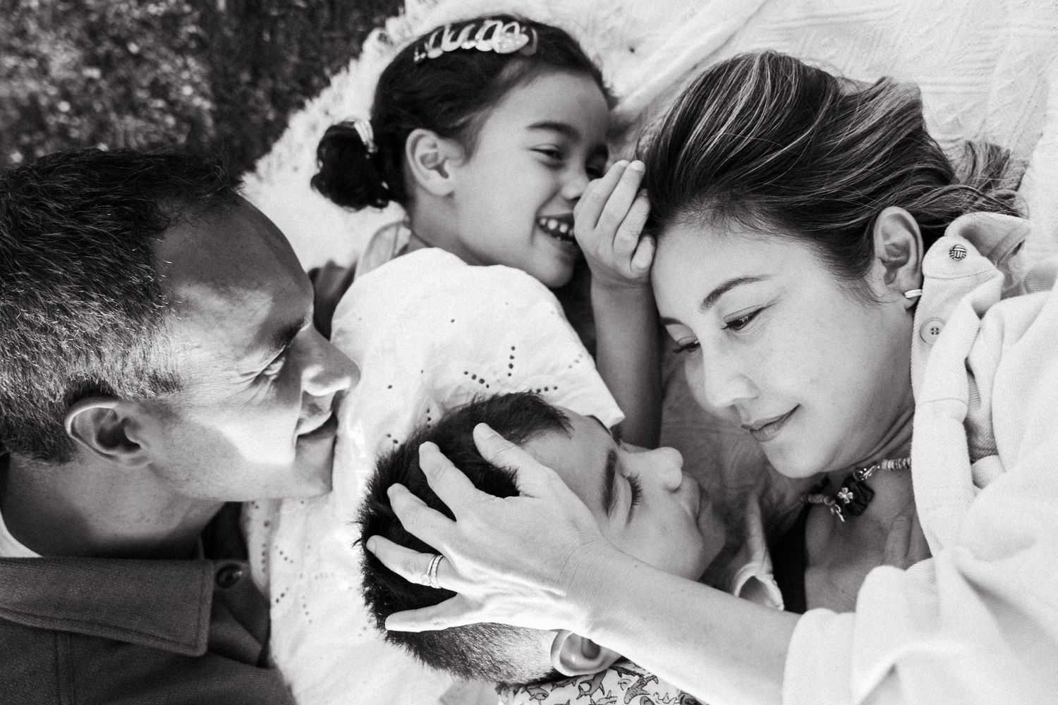 Black and white family photo of parents and two children laughing and cuddling together outdoors.