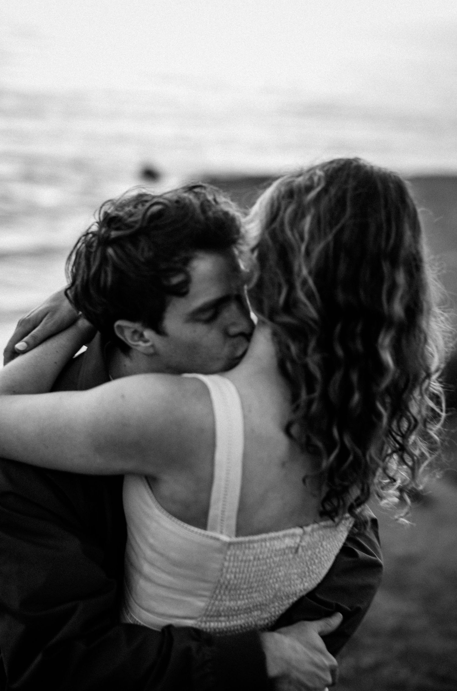 Couple sharing romantic kiss on beach in black and white photo.