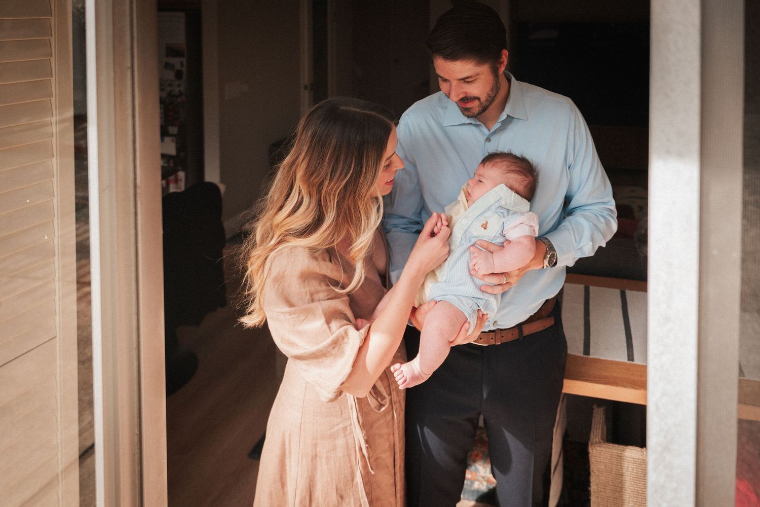 Happy couple sharing a tender moment with their newborn baby in a warm home doorway.