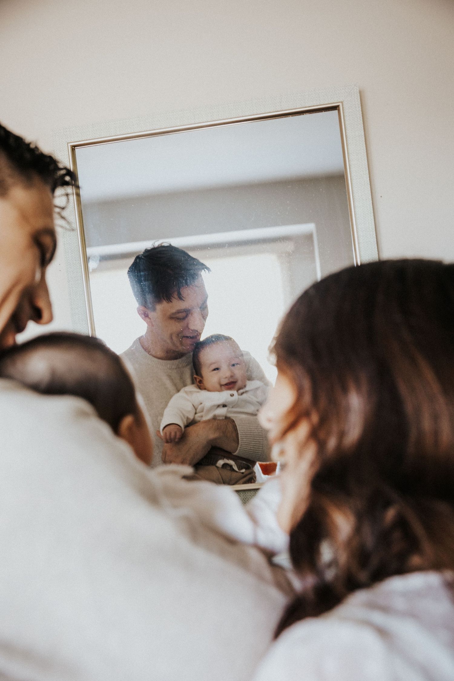 Young family with newborn baby reflected in mirror during intimate home portrait session.