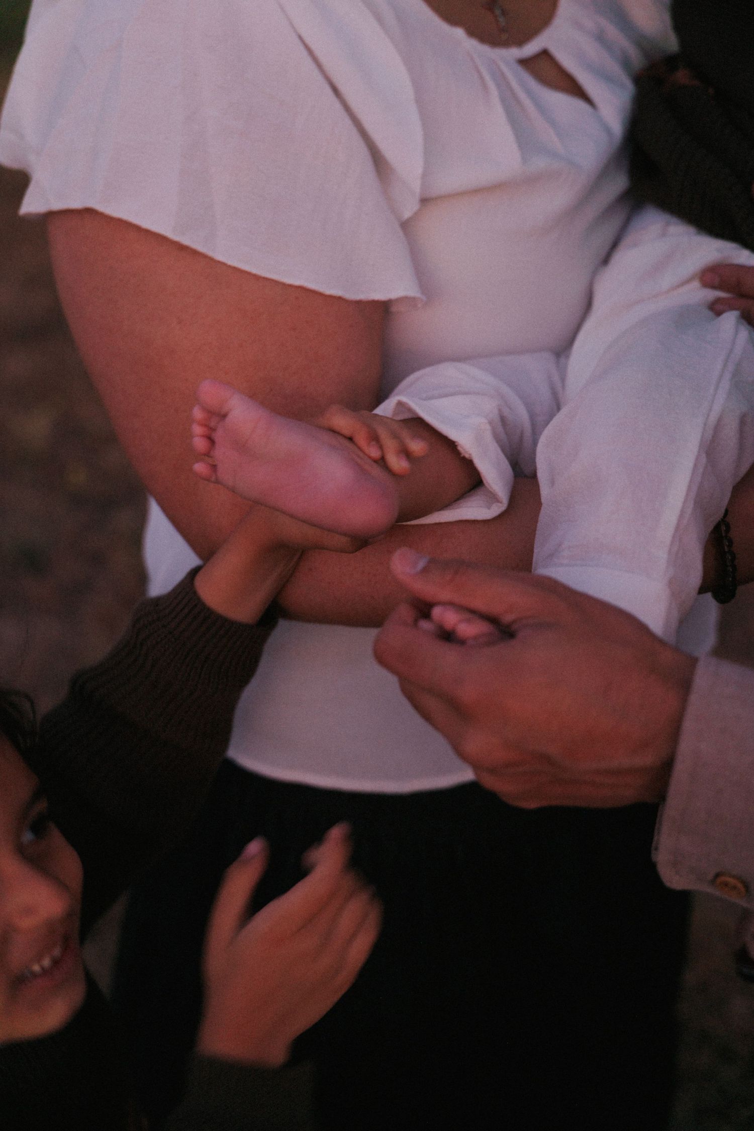 Close-up of adult hands gently holding a newborn baby's tiny feet during a family moment.