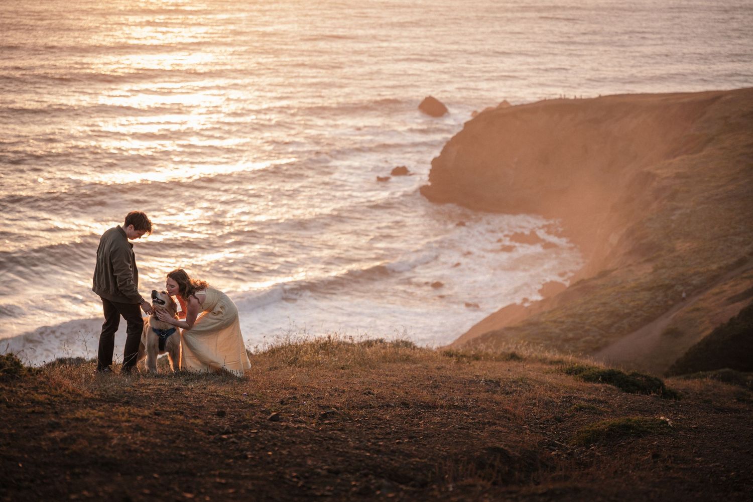 Couple standing on coastal cliffs at golden hour overlooking ocean waves below. Photography by The Y.K. Studio.