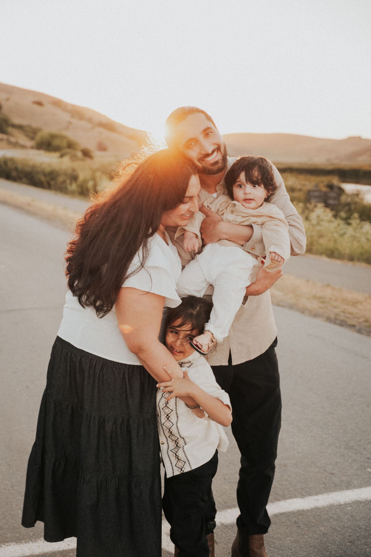 Family of four posing outdoors at golden hour with rolling hills and warm sunset light in the background.