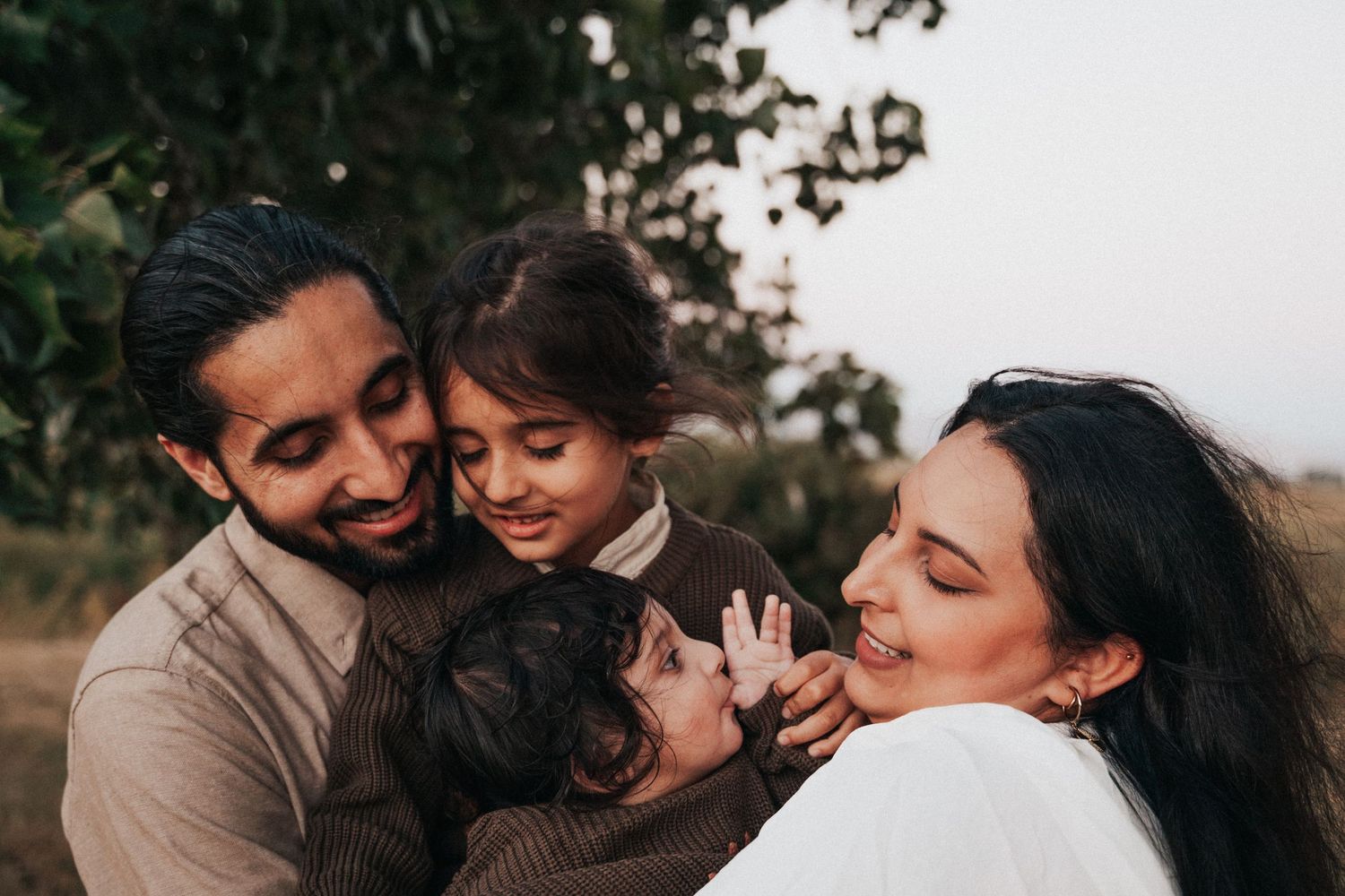 Happy family of four sharing a joyful embrace outdoors in a lush green setting.