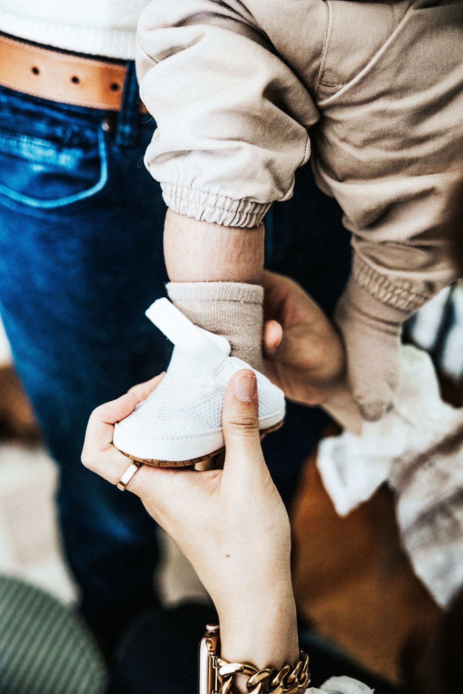 Mother placing white sneaker shoe on baby's foot held by father in close-up photo.