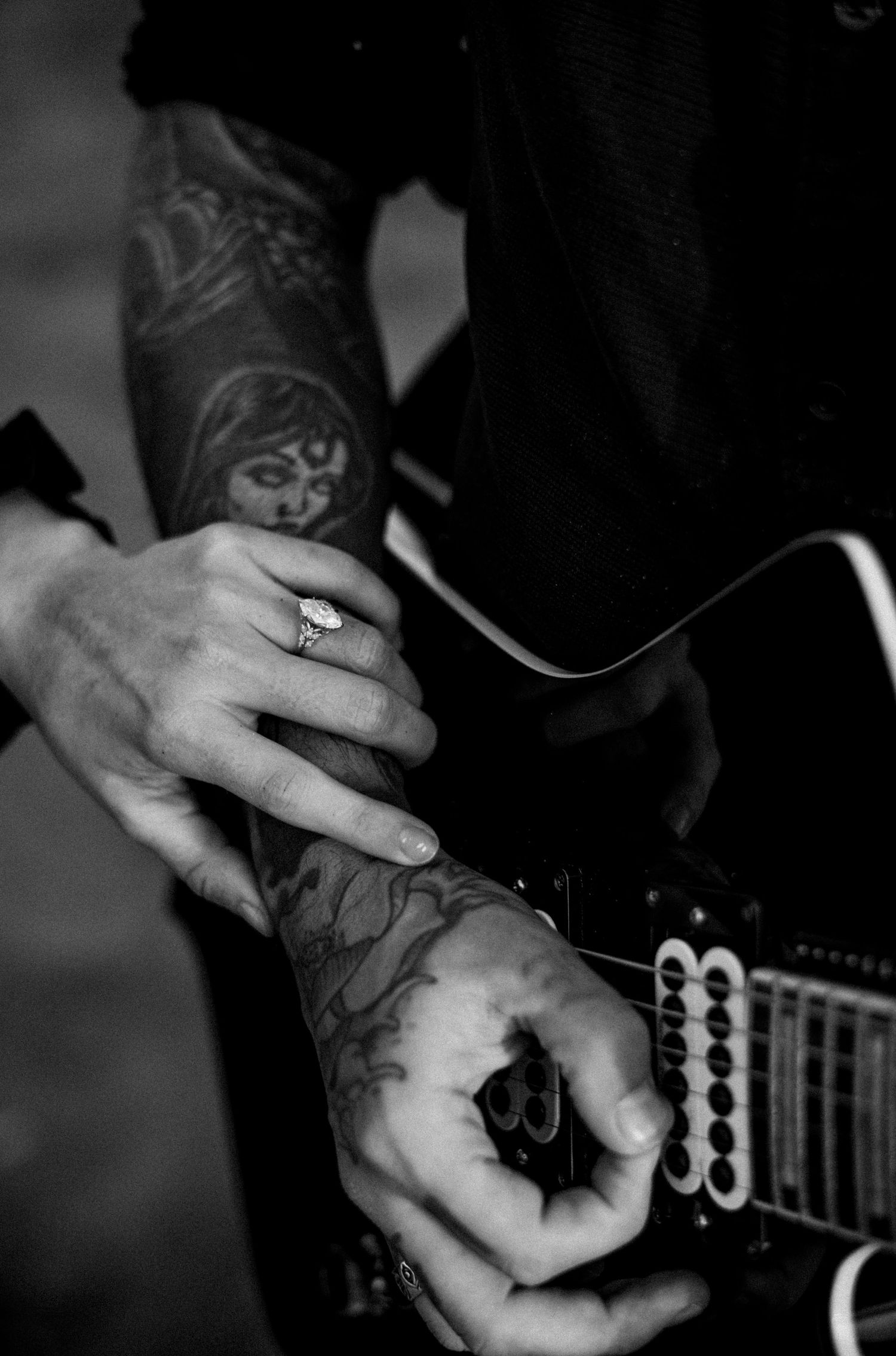 Tattooed hands on electric guitar with diamond engagement ring in black and white.
