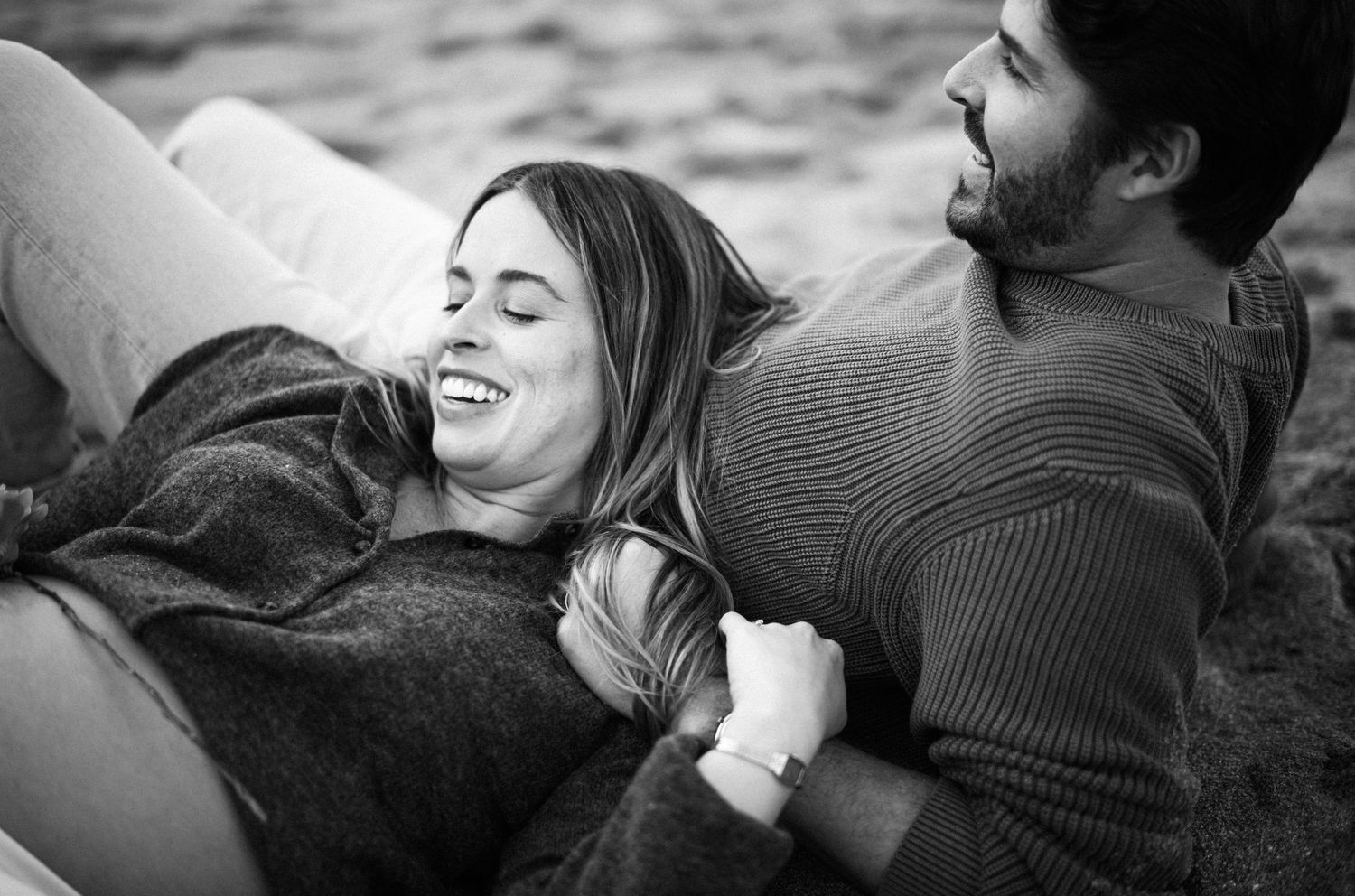 Black and white photo of a happy couple laughing and embracing while lying together outdoors.