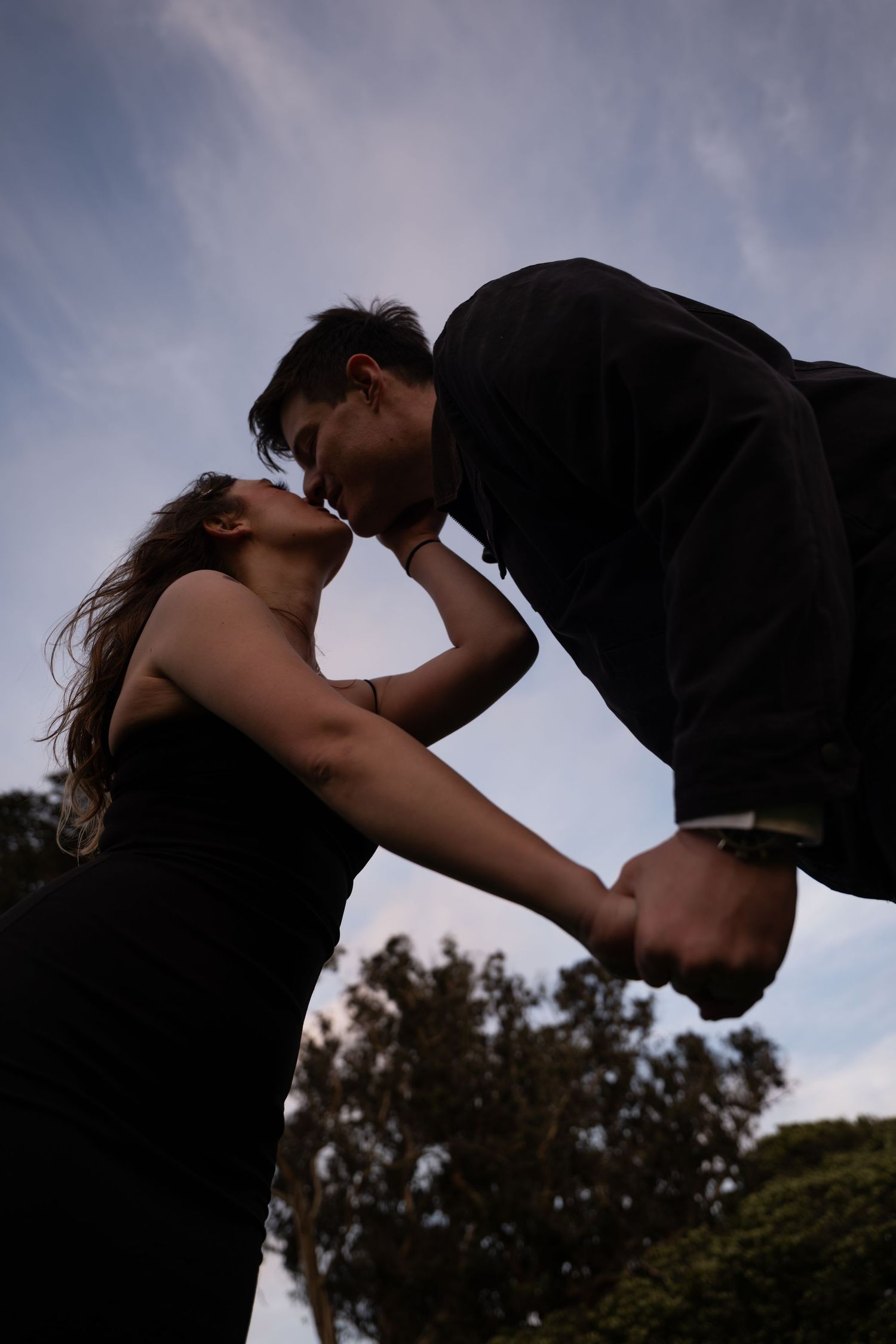 Silhouette of couple sharing a kiss against a dramatic cloudy sky at sunset.