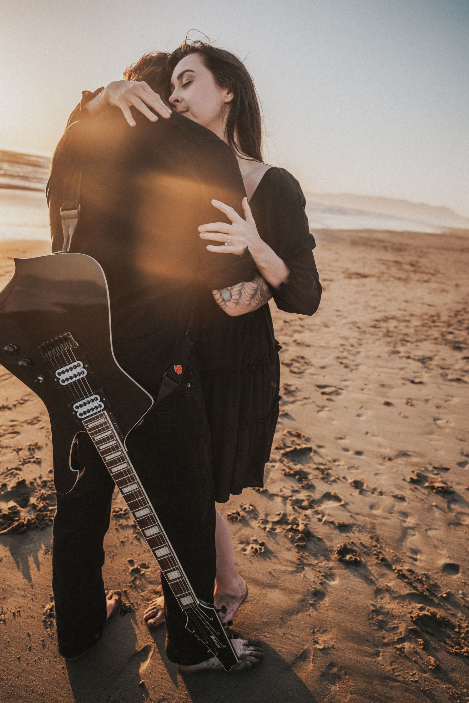 Couple embracing on a sandy beach at sunset with a black electric guitar, romantic outdoor photography.