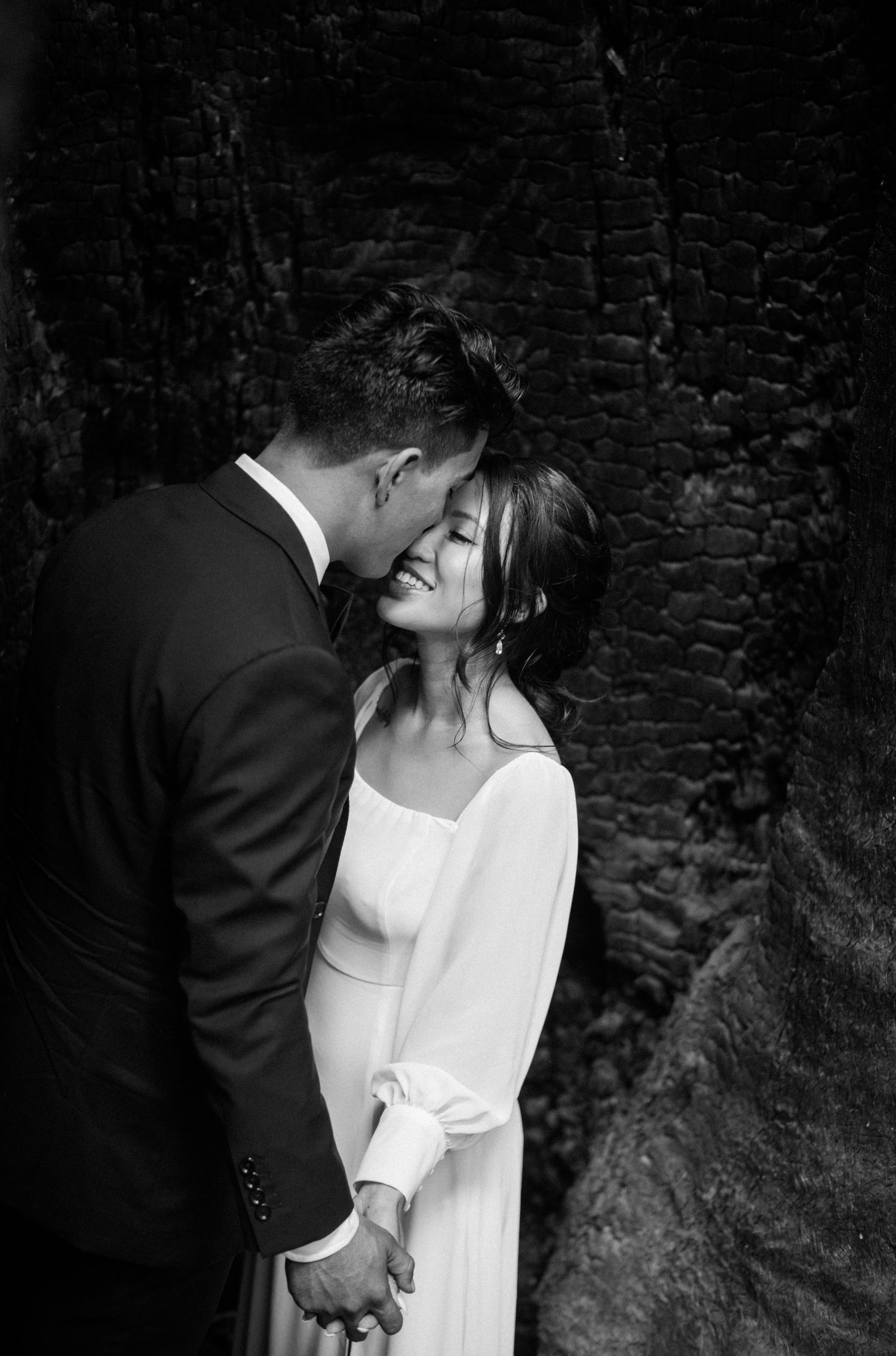 Black and white wedding photo of a couple sharing a tender moment, groom kissing bride's cheek as she smiles softly.